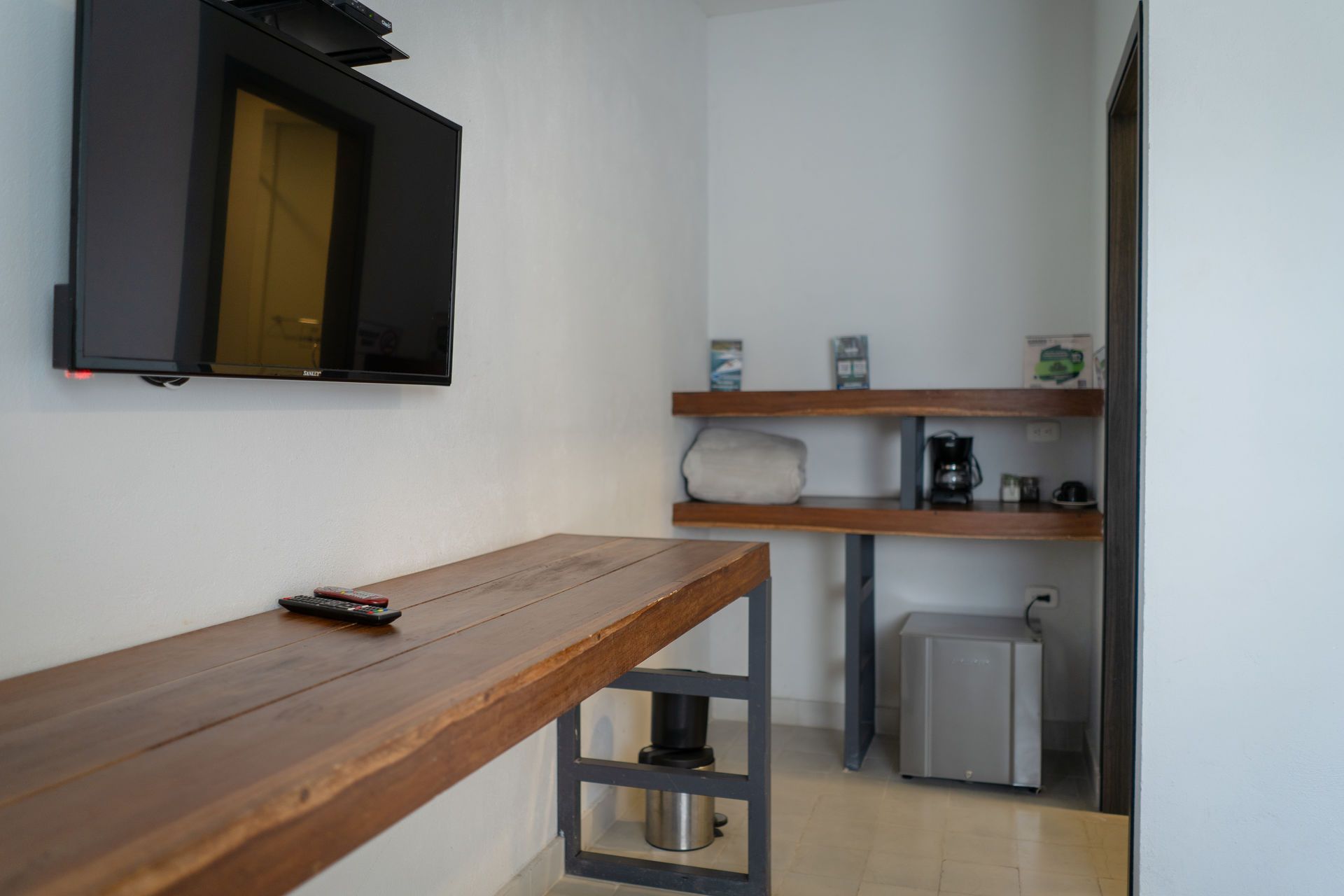 Habitación interior con TV, escritorio de madera, estanterías, cafetera y pequeño refrigerador.