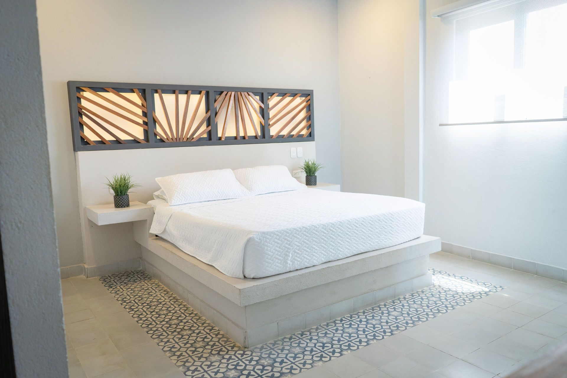 Dormitorio con cama, detalles en piso de guijarros y cabecera decorativa con paneles retroiluminados.