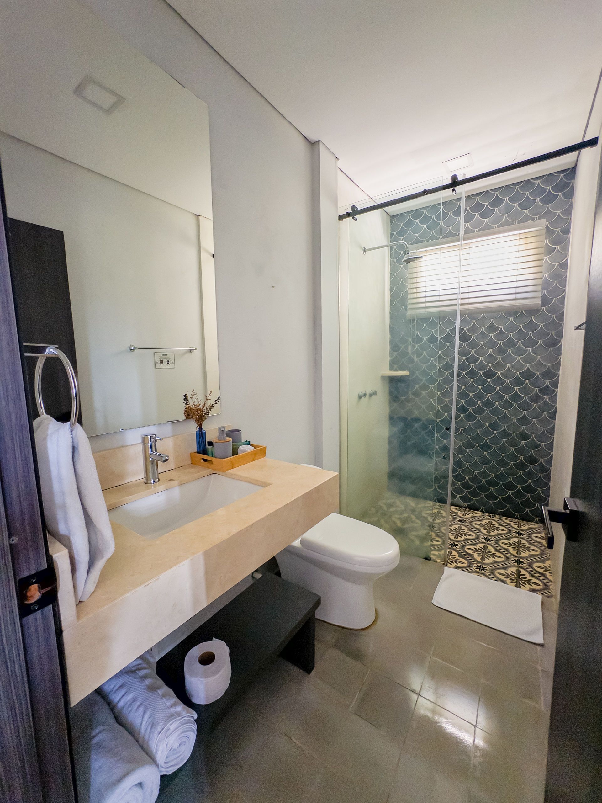 Baño moderno con tocador flotante, ducha de vidrio y piso de baldosas grises.