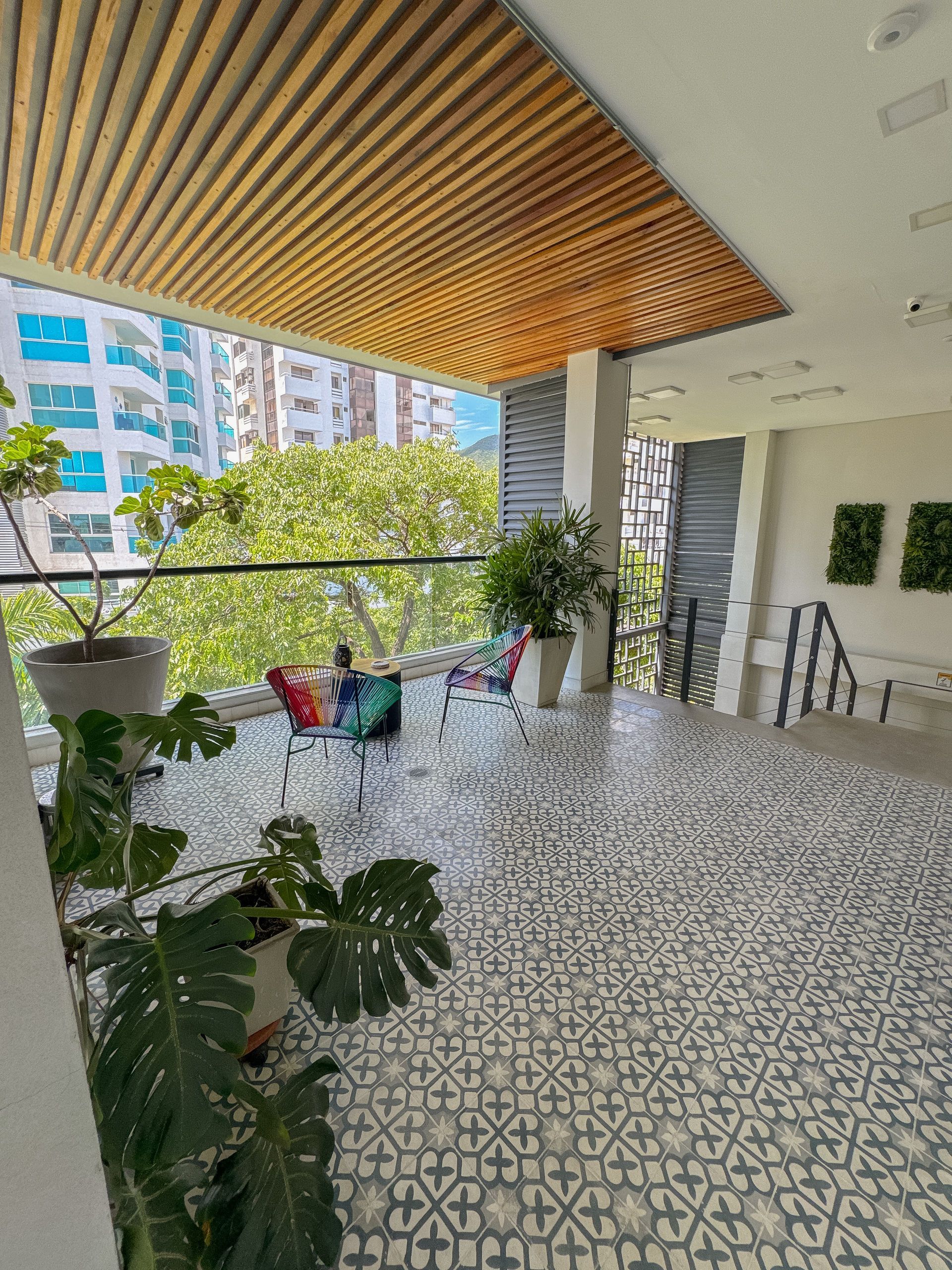 Balcón con piso estampado, techo de madera y plantas en macetas, con vista a los edificios de la ciudad.