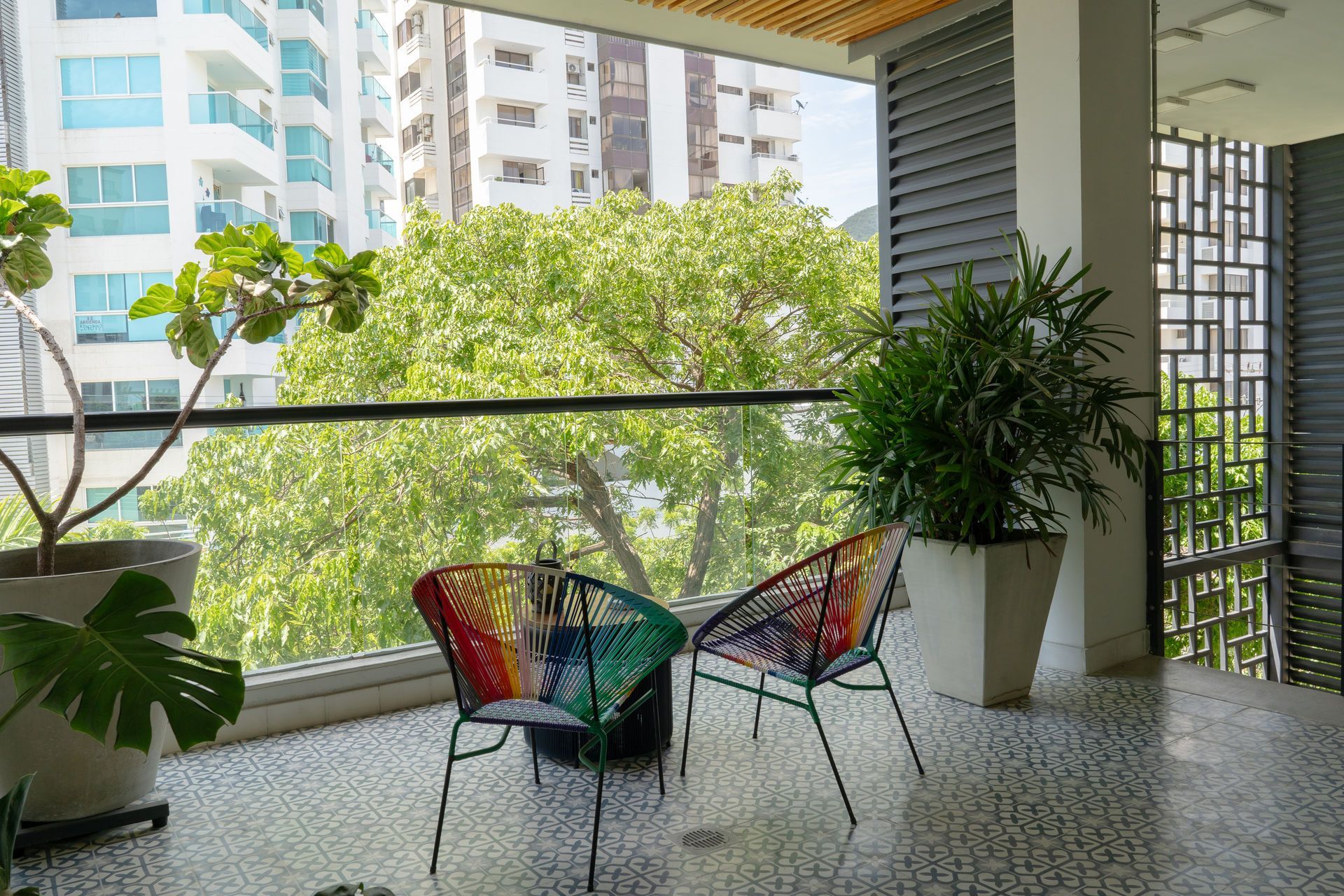 Balcón con dos sillas tejidas de colores, plantas en macetas y vista a la ciudad.