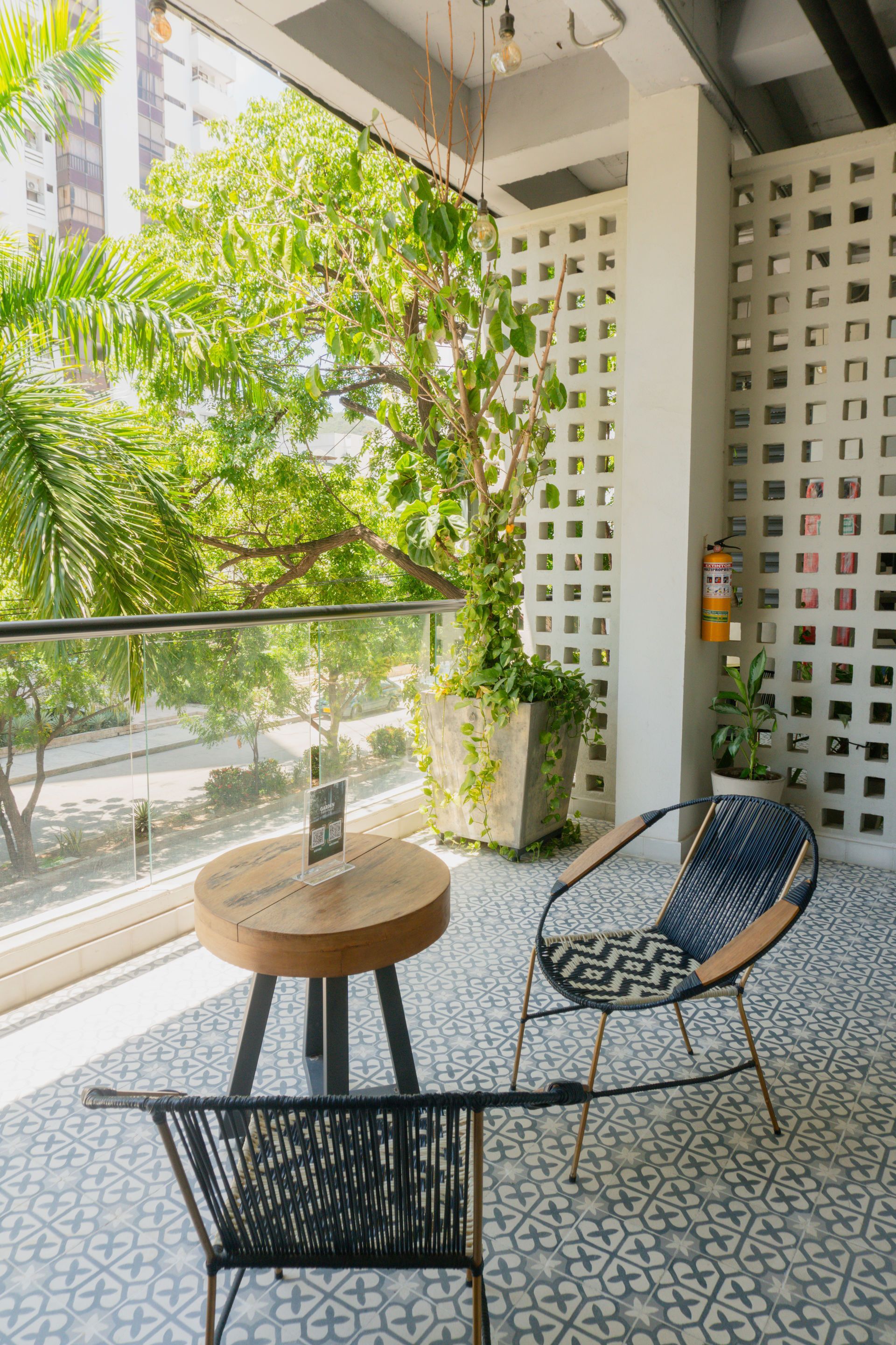 Zona de estar al aire libre con mesa redonda, dos sillas y una pared blanca texturizada, con vista a la vegetación.