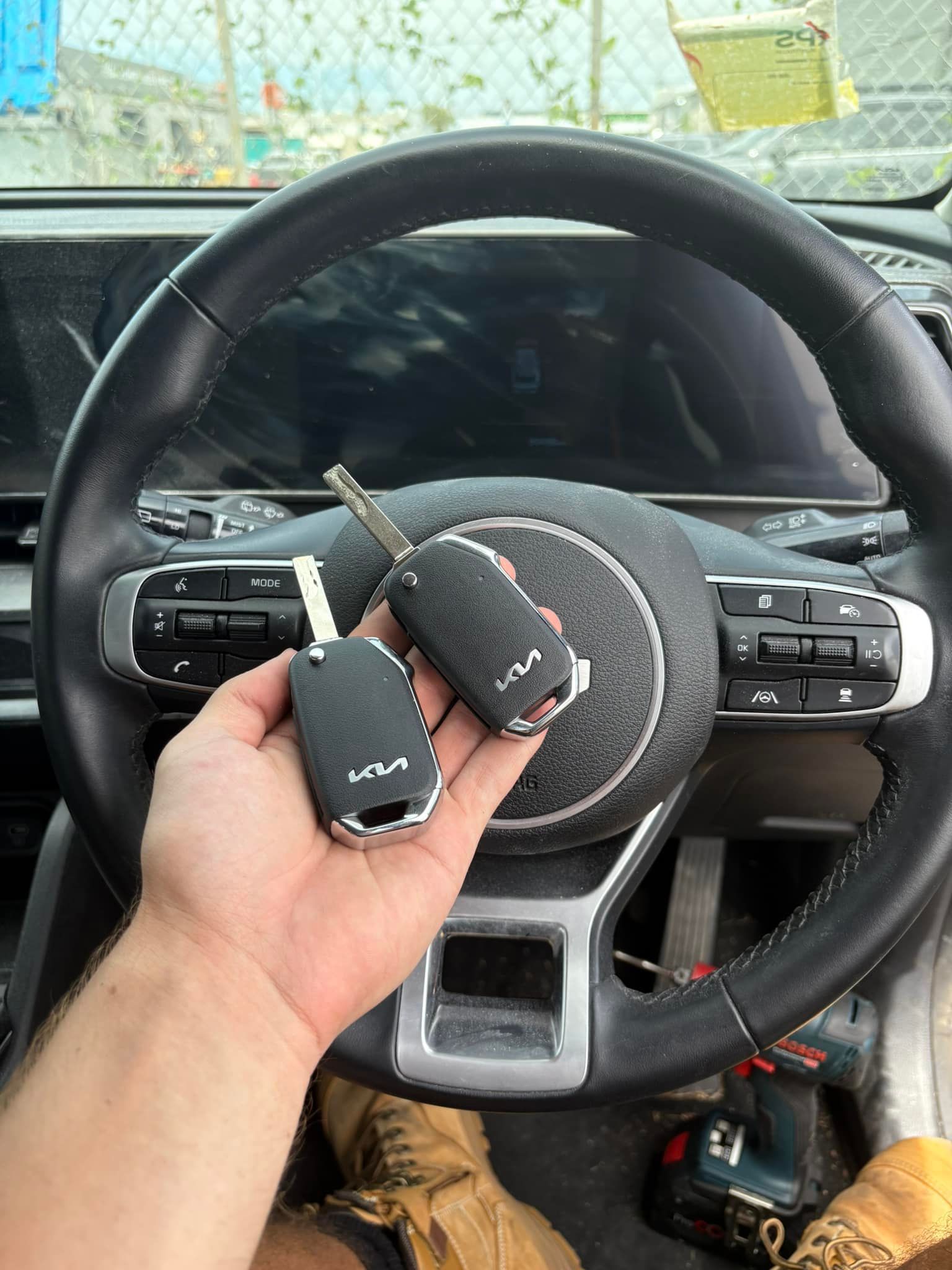 Hand Holding Two Kia Car Keys in Front of A Steering Wheel — Nq Locksmiths In Kirwan, QLD