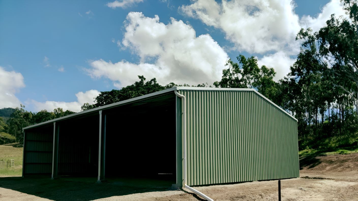 A Green Metal Building is Sitting on Top of a Dirt Hill — Mareeba Sheds & Gas In Mareeba, QLD