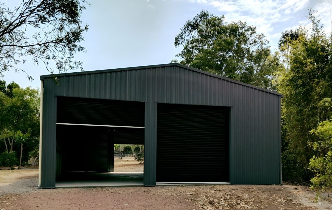 A Black Metal Garage With Two Garage Doors is Surrounded by Trees — Mareeba Sheds & Gas In Mareeba, QLD