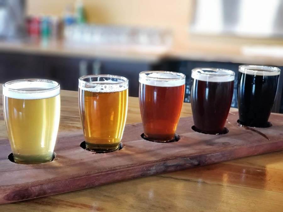 Five glasses of beer are lined up on a wooden tray.