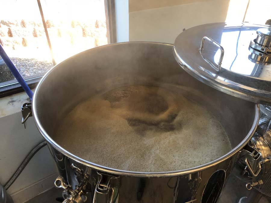 A large stainless steel pot is filled with liquid and steam coming out of it.