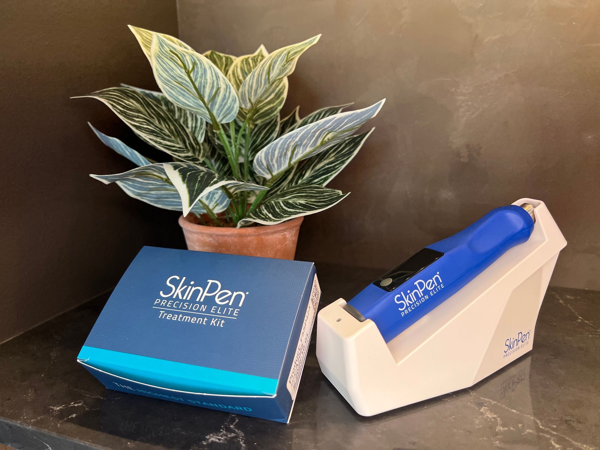 SkinPen micro-needling device and box set on a dark counter next to a potted plant.