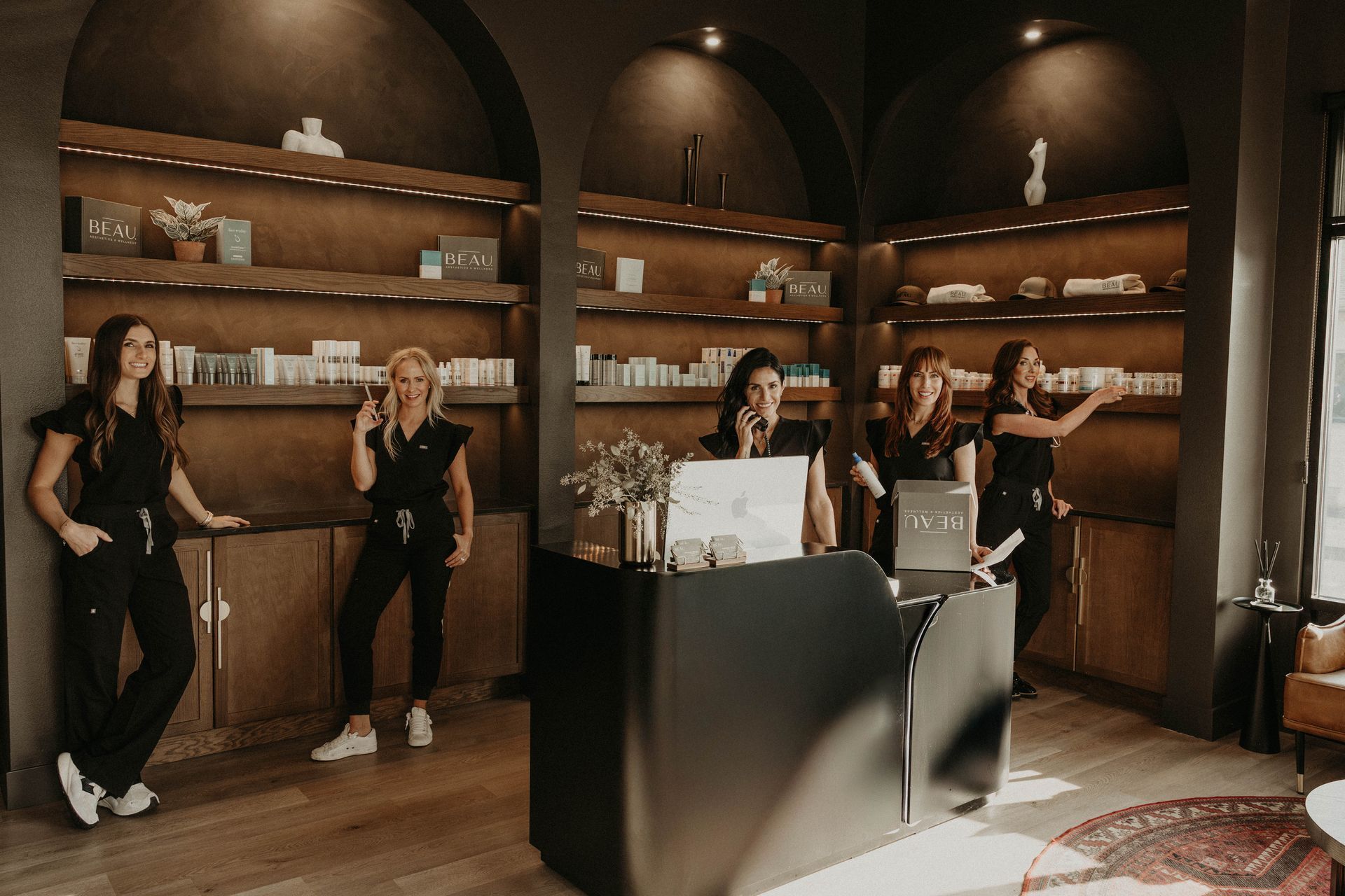 Five people in black scrubs stand in a dark, modern office with shelves of products.