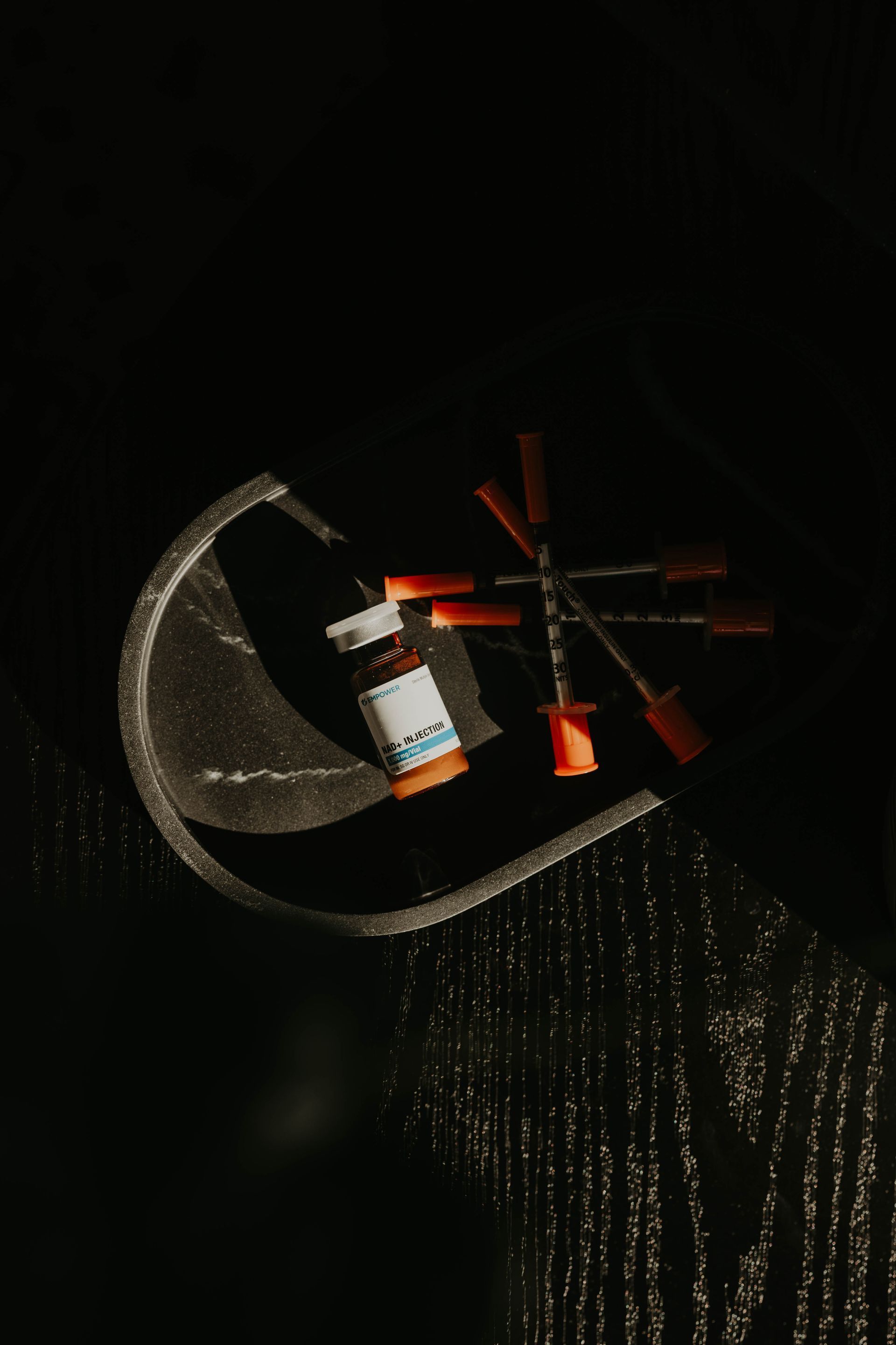Vial of medicine and several syringes on a dark surface, lit by sunlight.