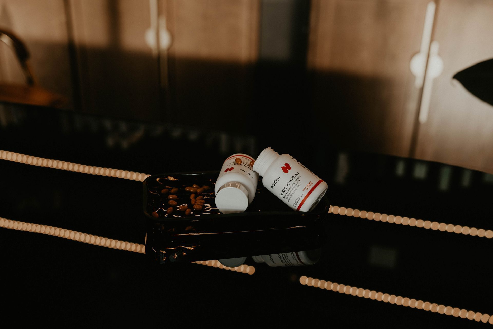 Two white pill bottles with red crosses on a shiny black surface with reflected lights.