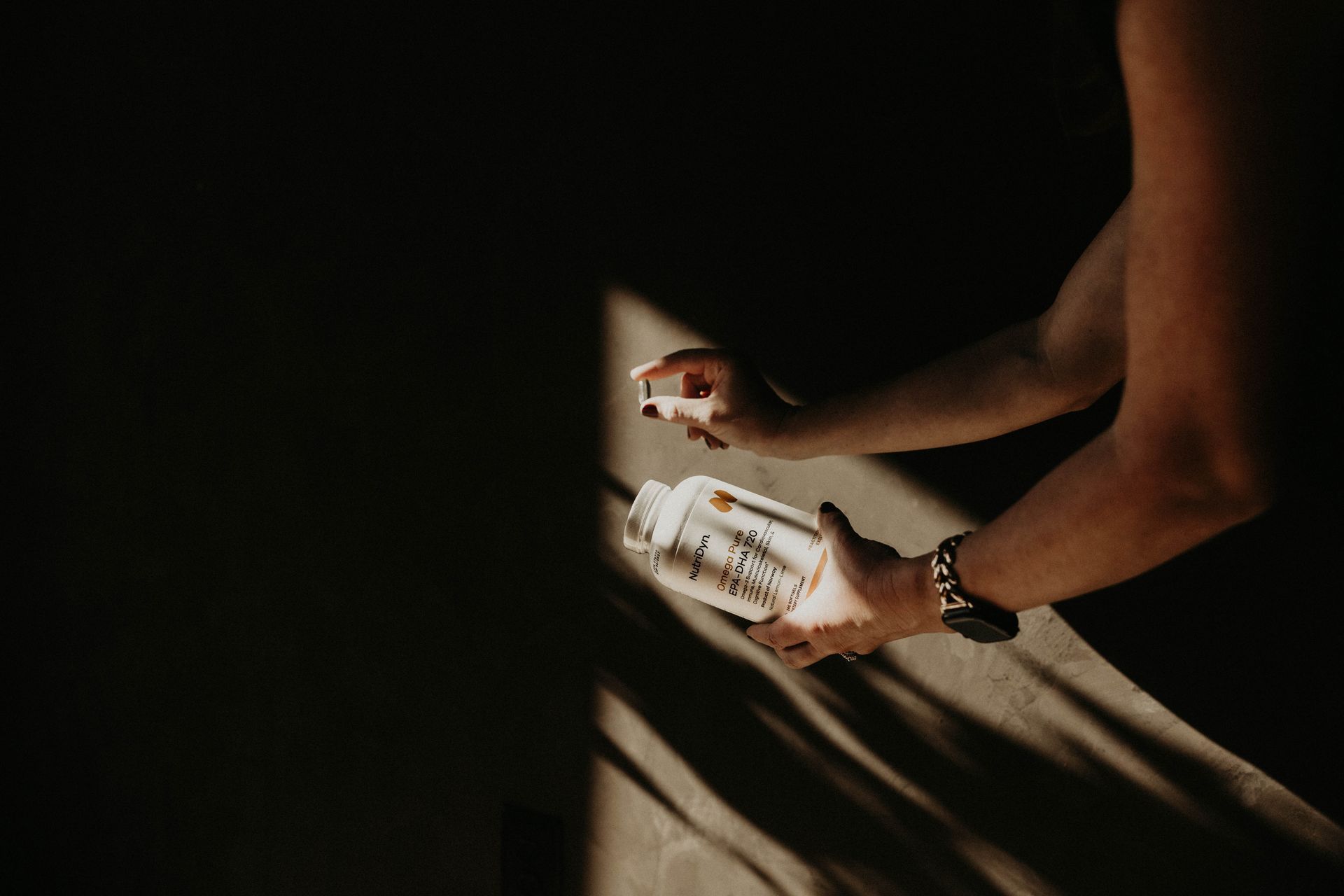 Person holding a supplement bottle, spraying something. Harsh shadows, warm light.