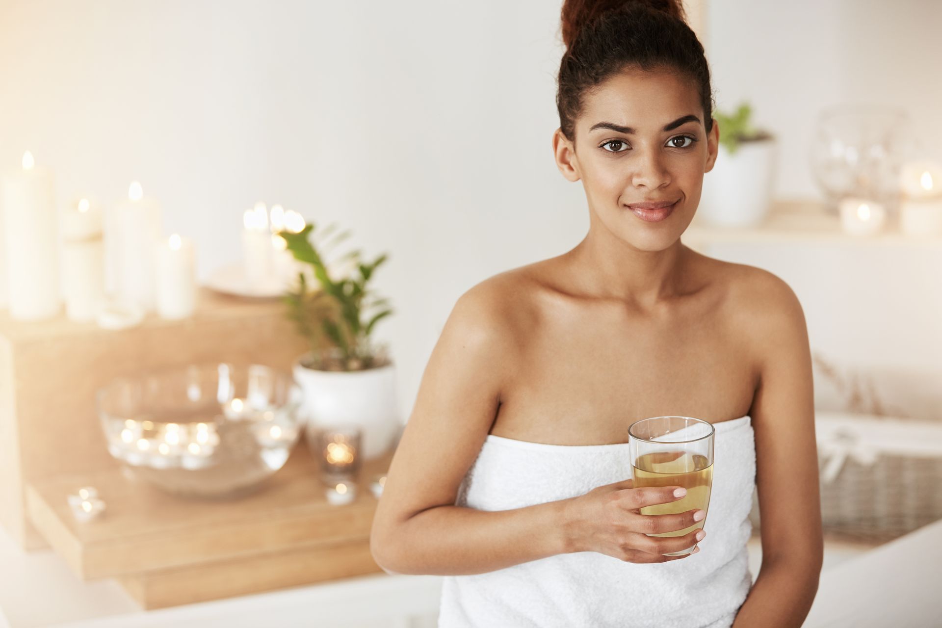 A woman wrapped in a towel is holding a glass of wine in a bathroom.