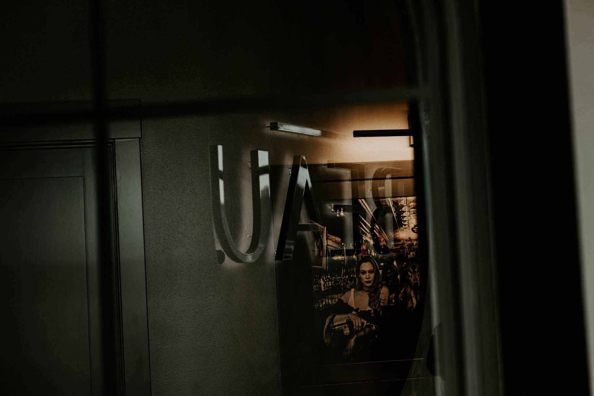 Reflection in a window reveals a poster of figures with warm lighting in a dark space.