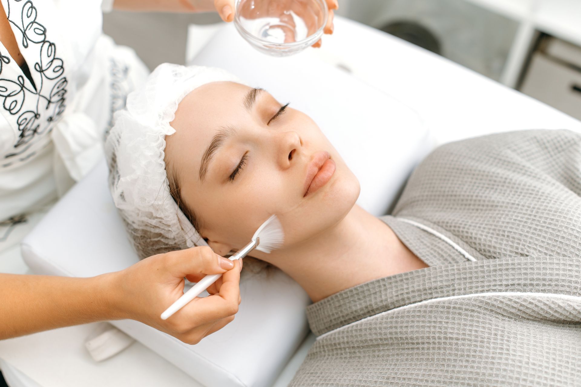 Spa esthetician applying facial treatment to a relaxed client lying on a treatment bed