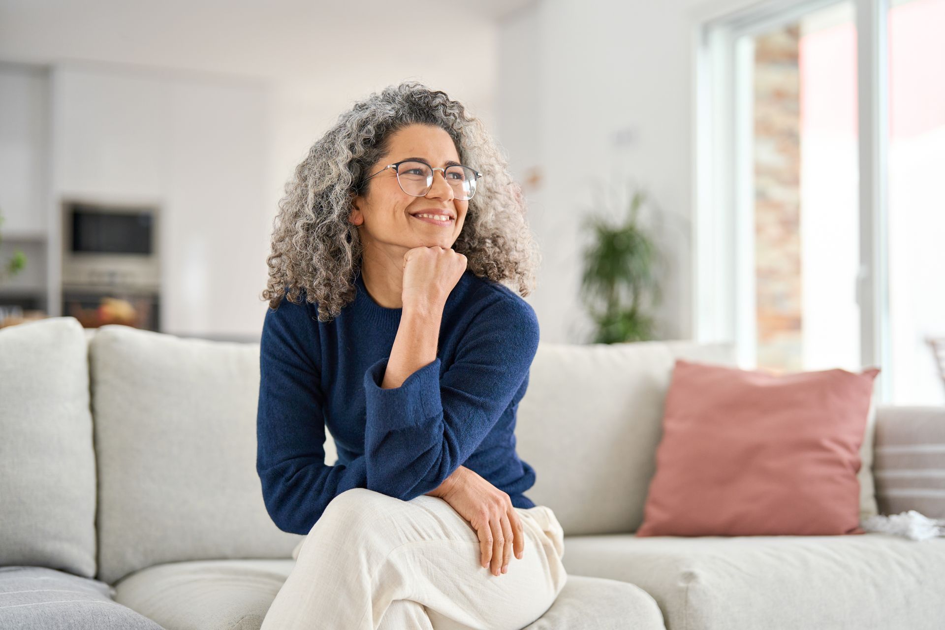 Smiling woman sitting on a light sofa in a bright living room with a pink pillow nearby