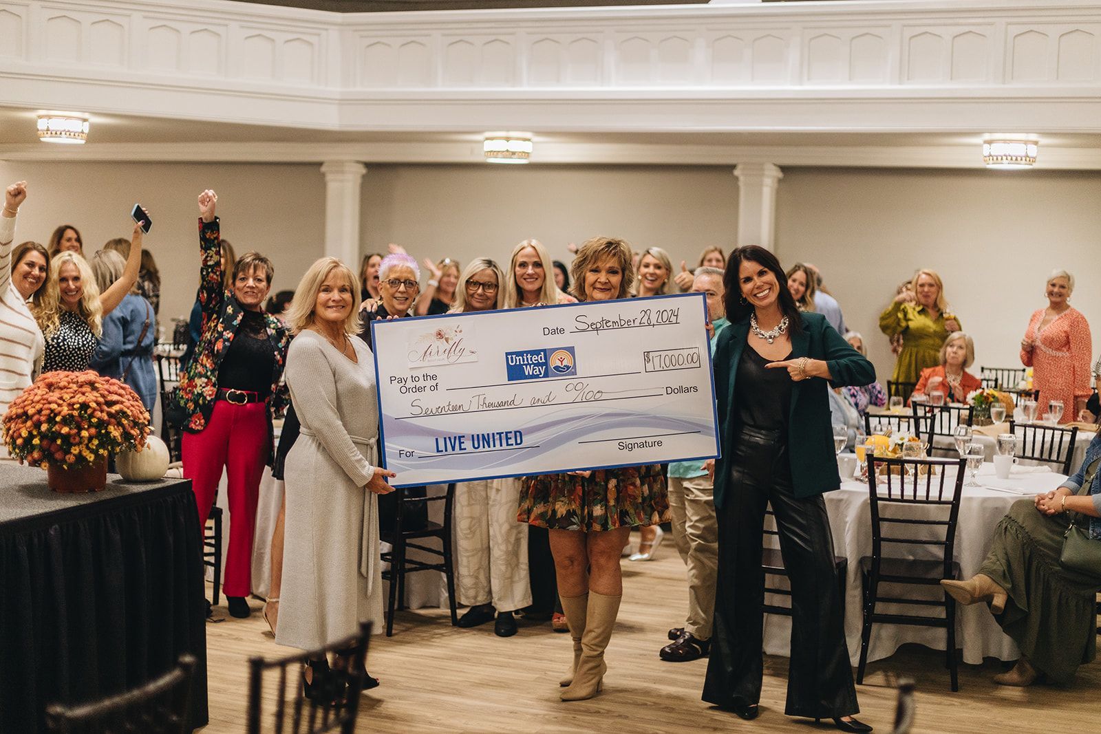 A group of women are standing in a room holding a large check.