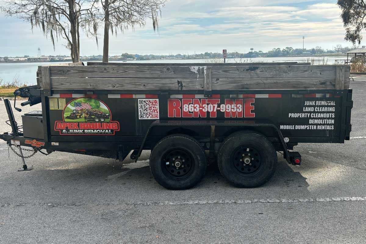 Black utility trailer with dark wheels and side graphics parked on pavement, overlooking water.