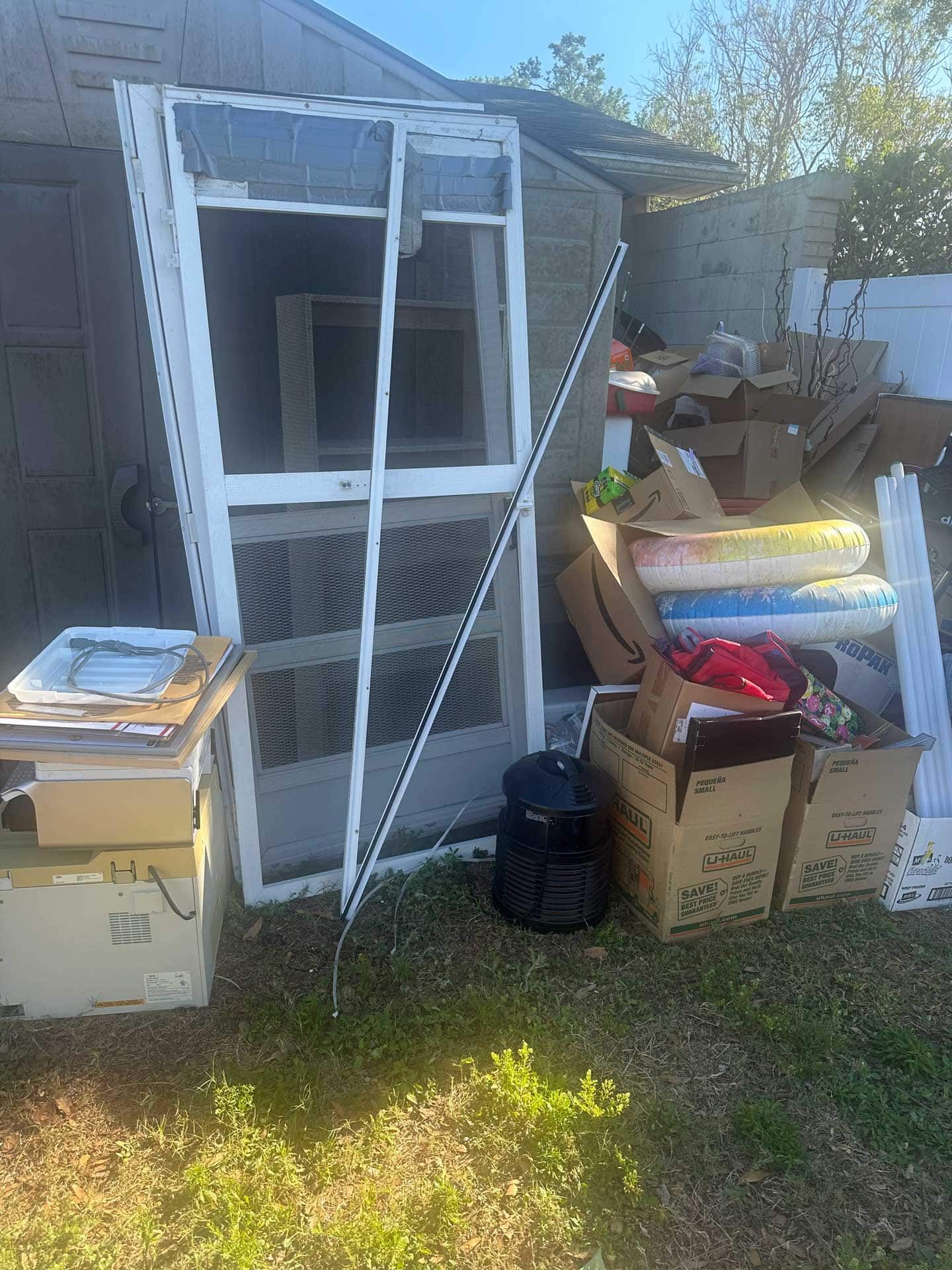 Pile of discarded items, including window frames, boxes, and a measuring stick, on grass.