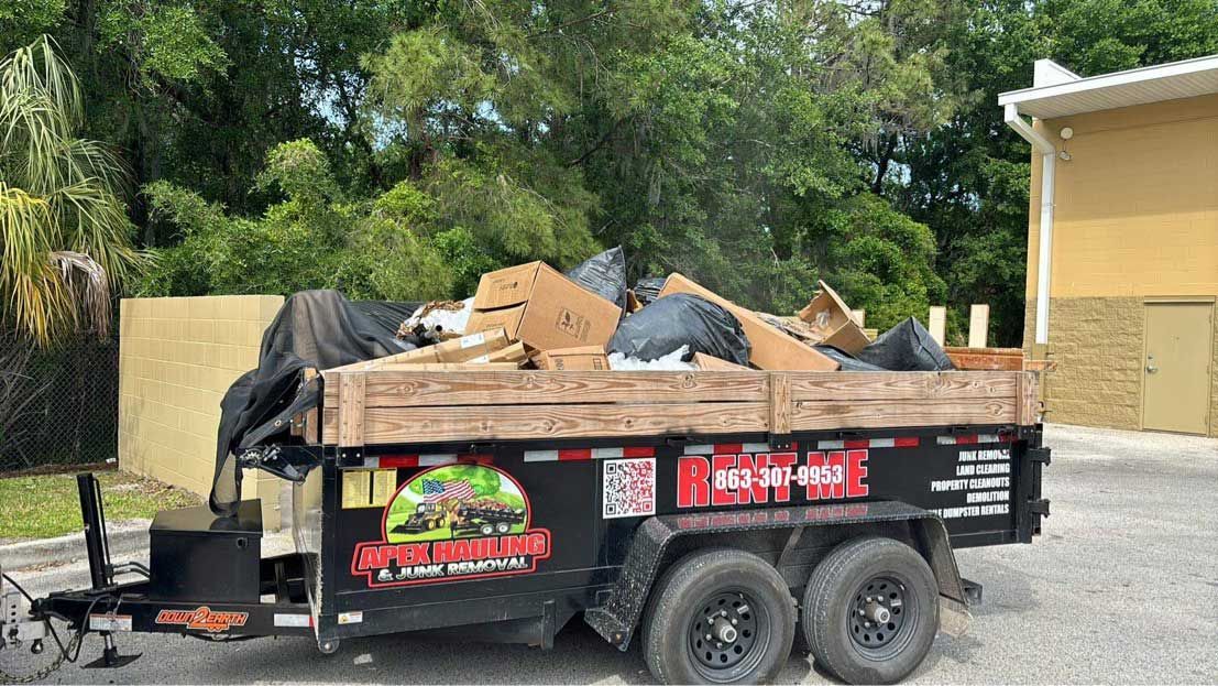 Trailer loaded with trash, cardboard, and bags; parked near a building with trees in the background.