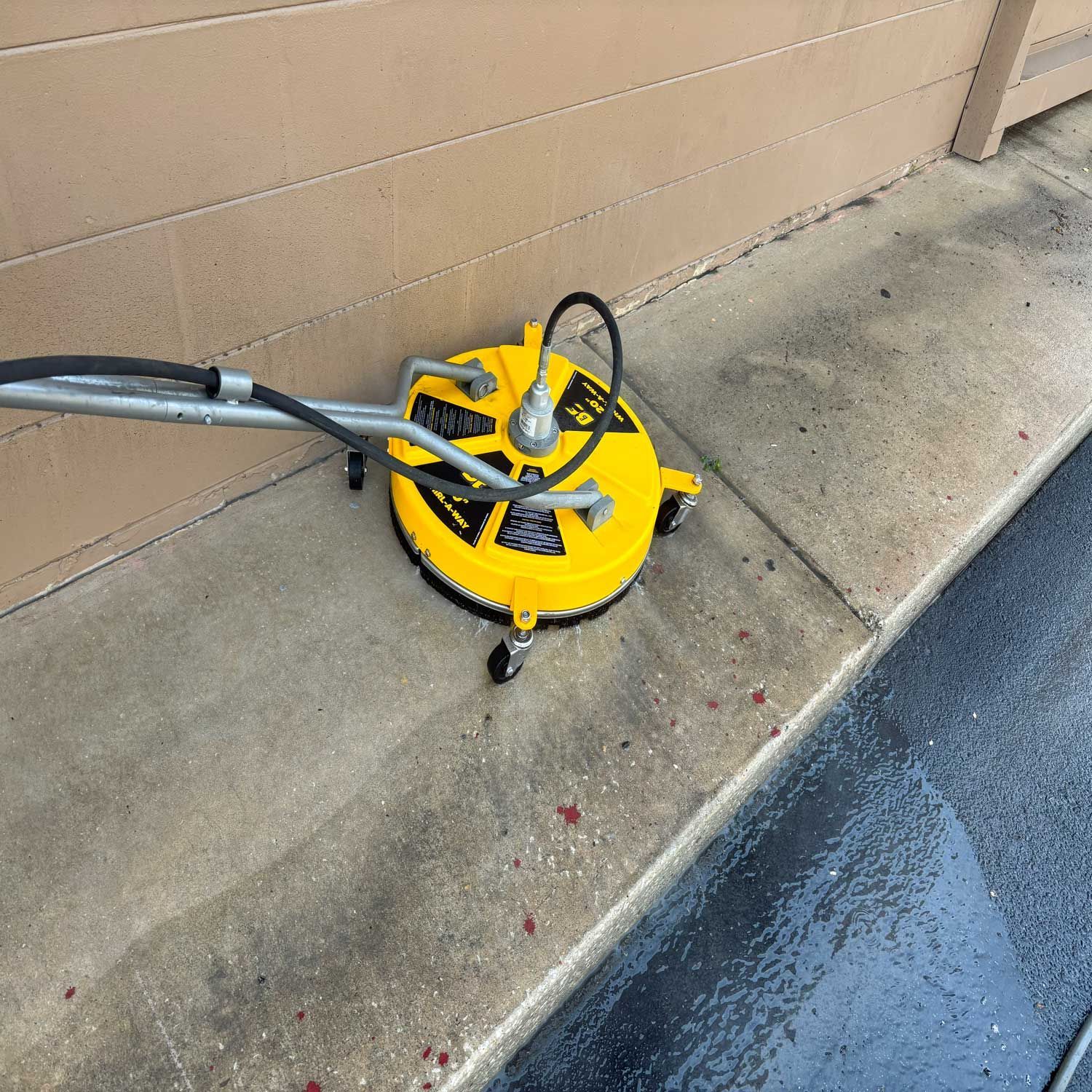Yellow surface cleaner on concrete next to building, cleaning.