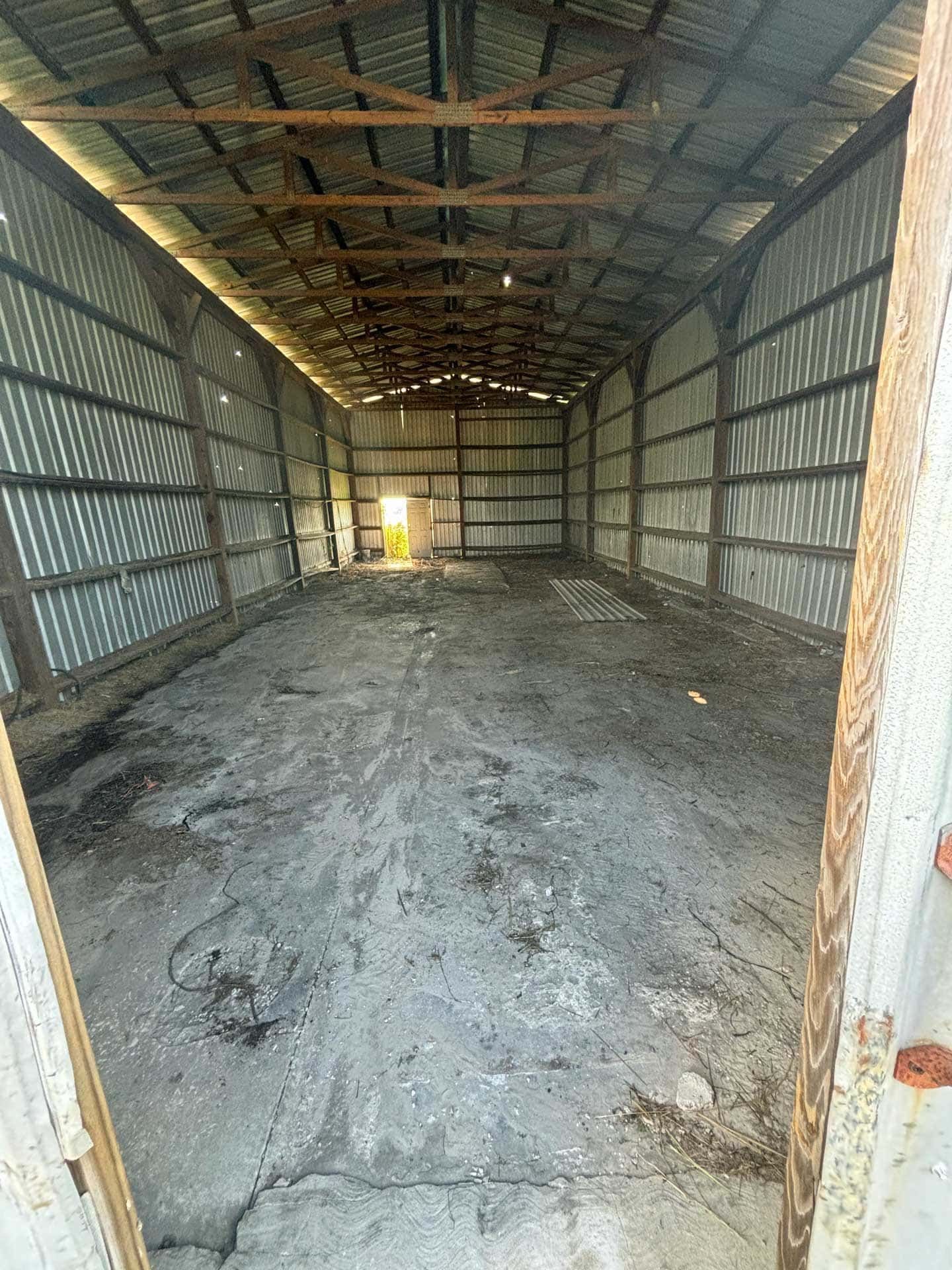 Empty corrugated metal building with dirt floor and open door at end.