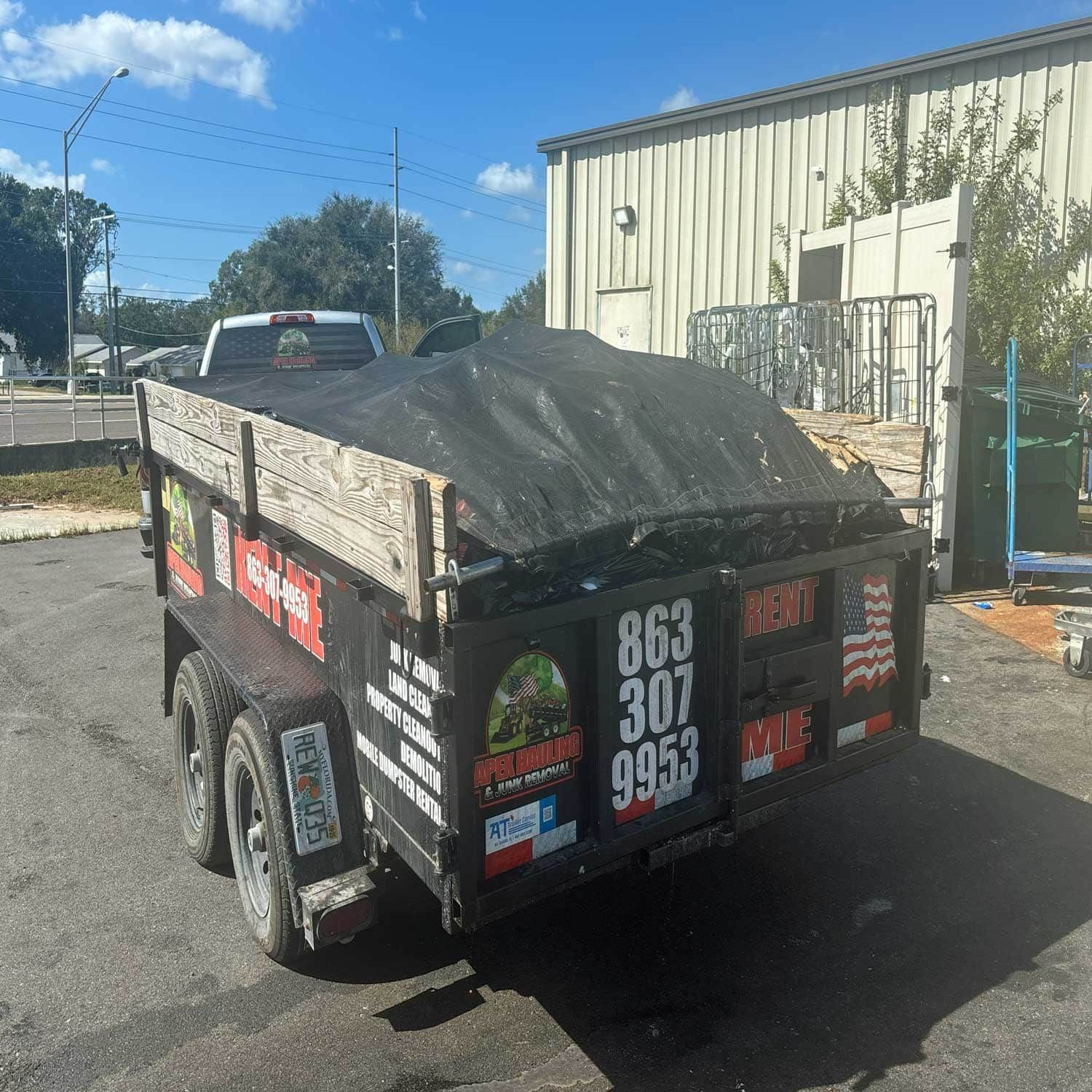 A trailer loaded with debris with a black tarp. The trailer has a phone number on it.