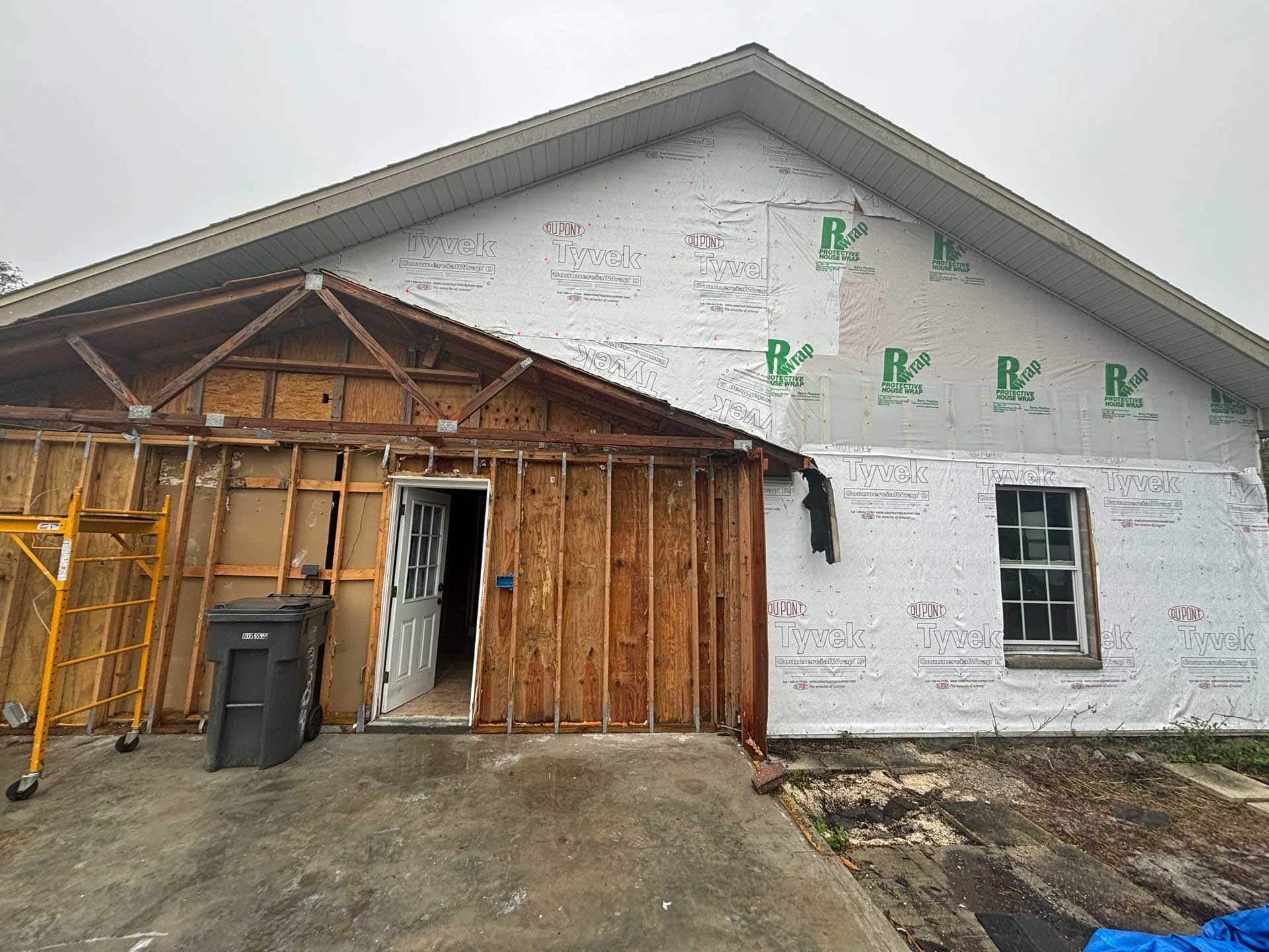 House exterior under construction, with exposed wood framing, wrap, and a window.