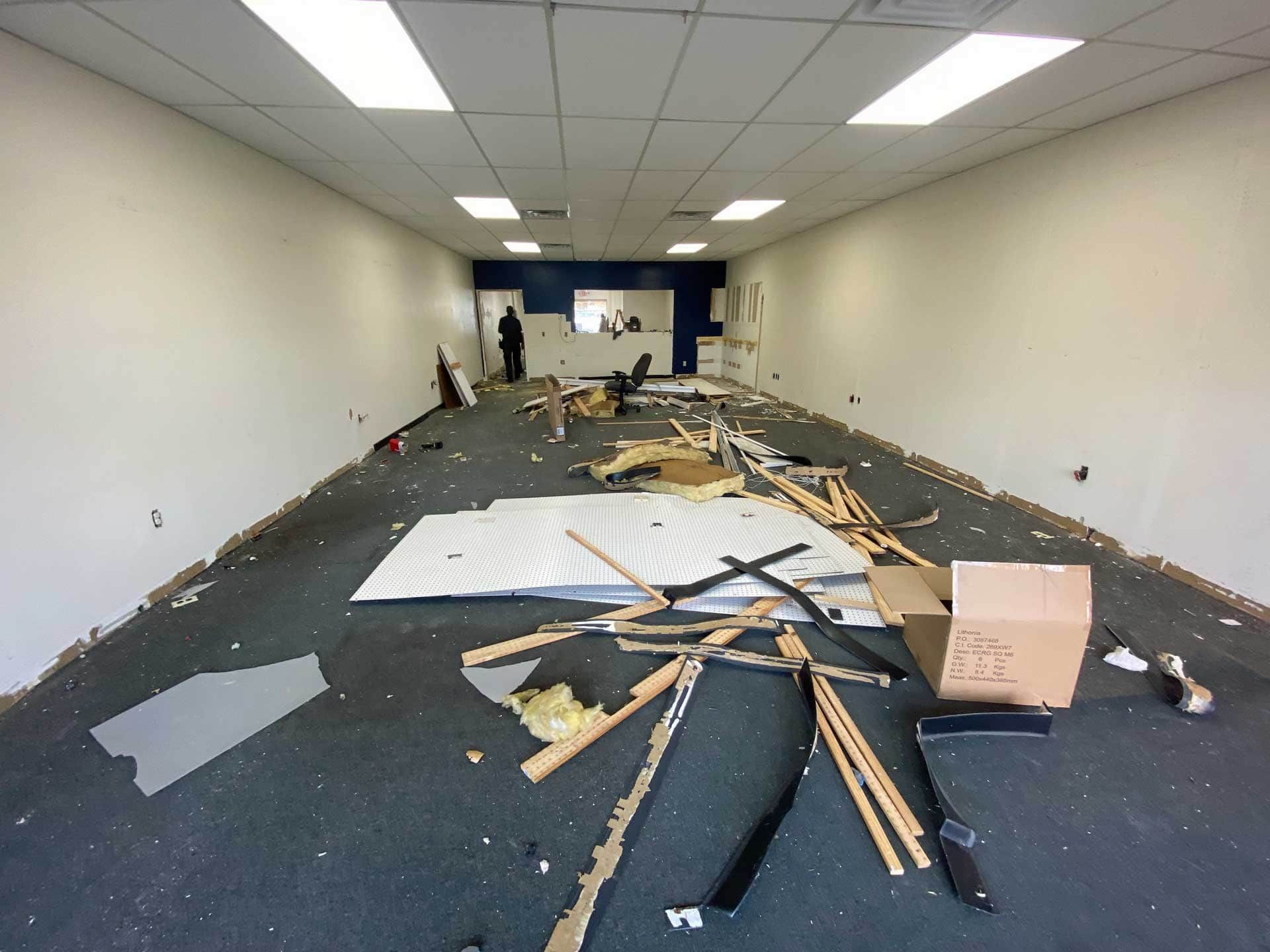 Interior of a demolished space, debris scattered on the floor. A person stands near the back wall.