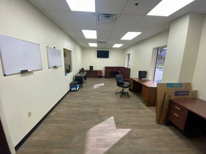 Empty office space with desks, whiteboards, and brown flooring.