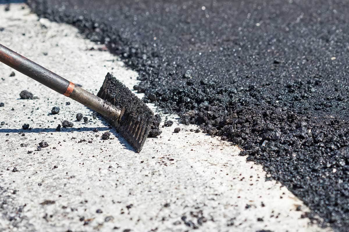Asphalt being spread on concrete surface with a brush.