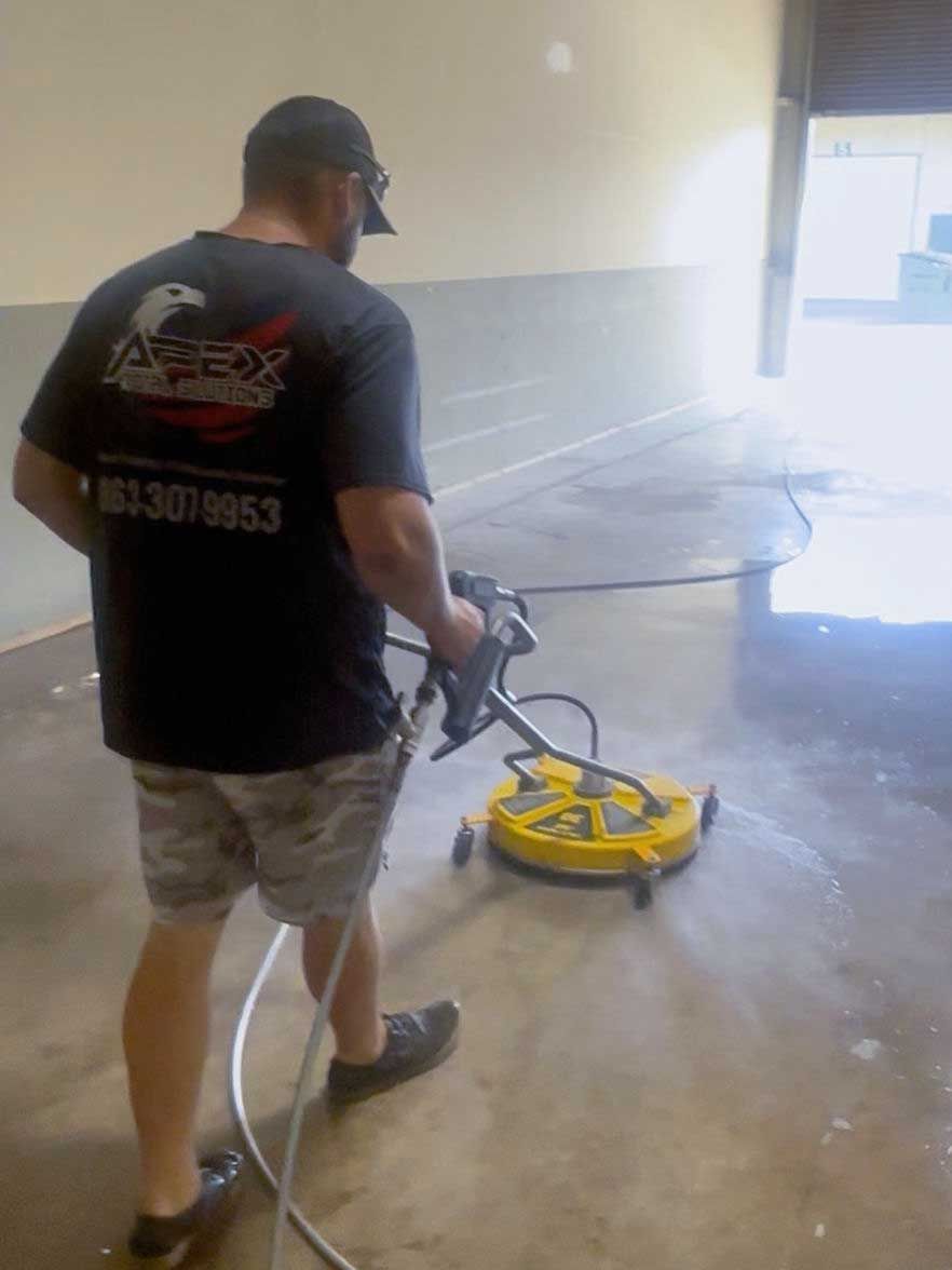 Man using a surface cleaner on a concrete floor in an industrial space.
