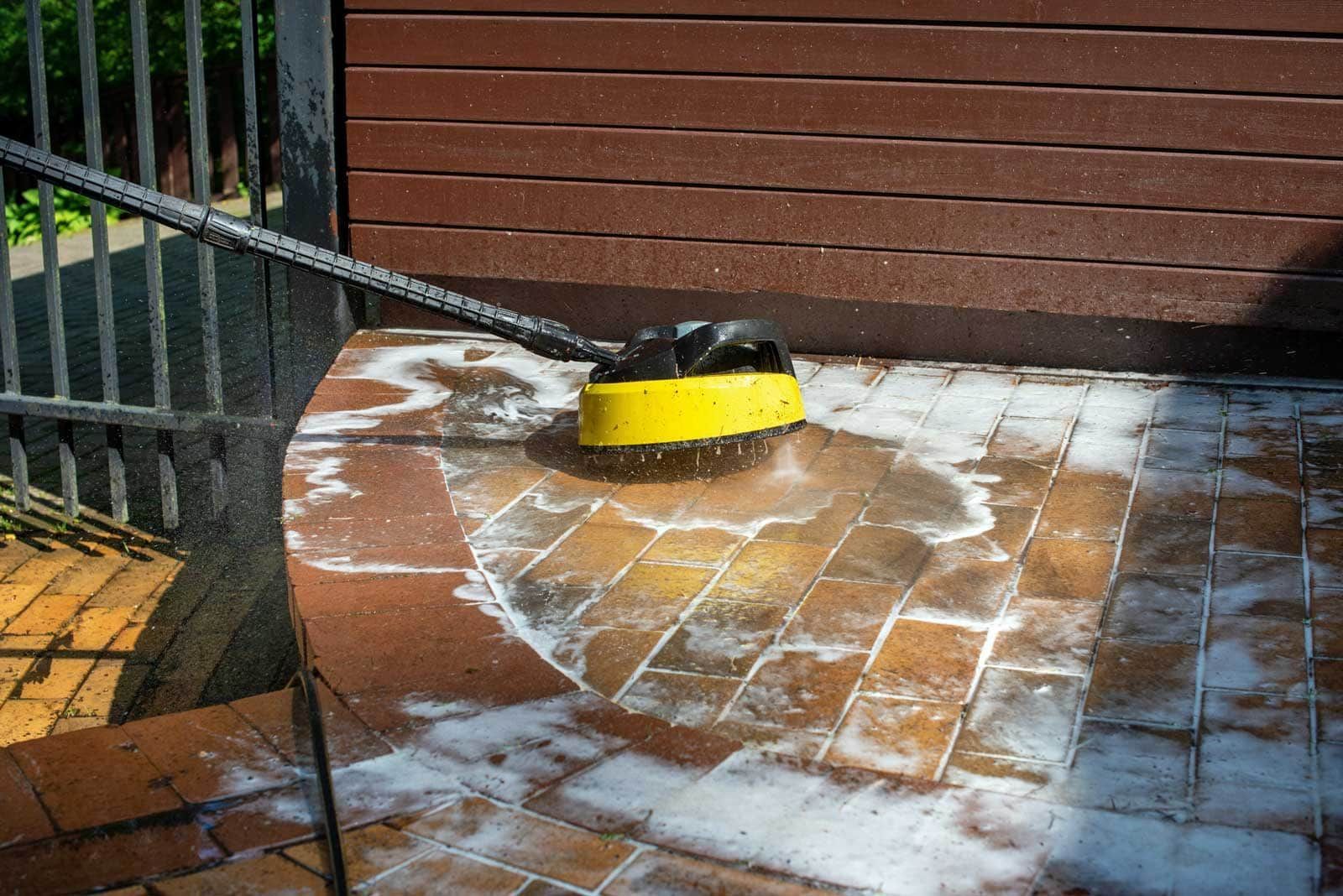 Yellow brush scrubbing brick patio with soapy water.