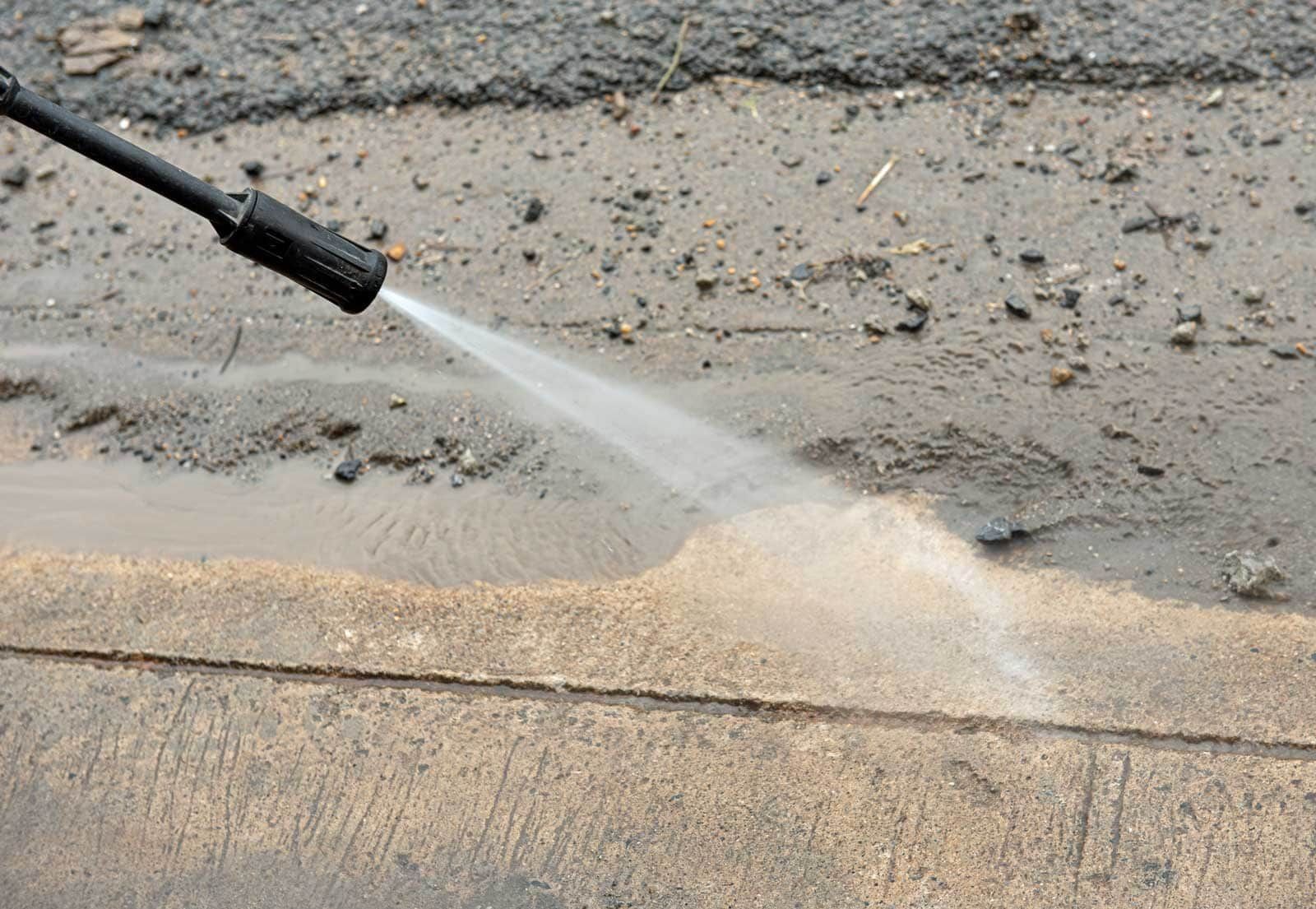 A pressure washer sprays water onto a concrete surface, removing dirt and debris.