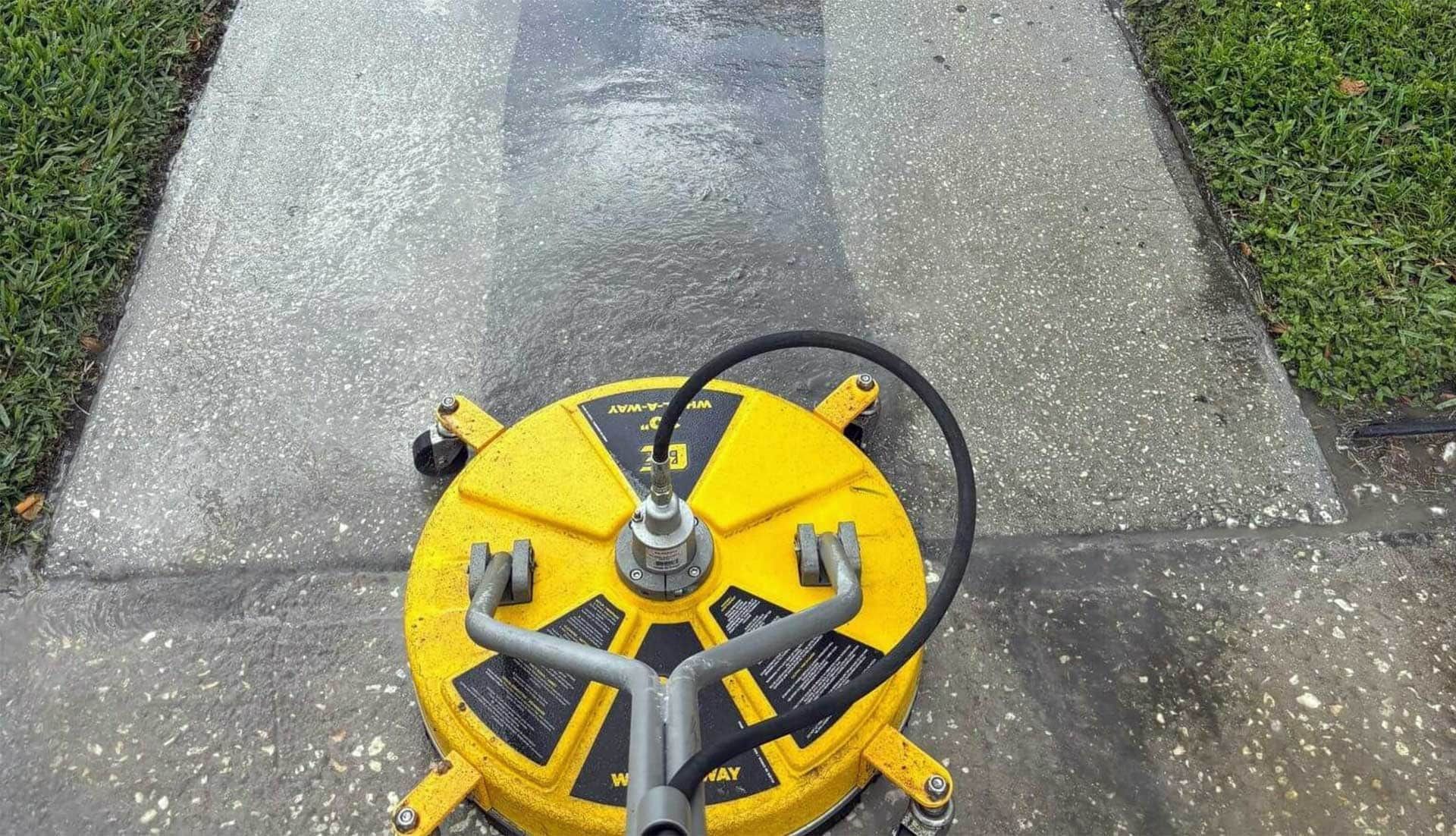 Yellow and black surface cleaner on a concrete sidewalk, removing dirt and grime.