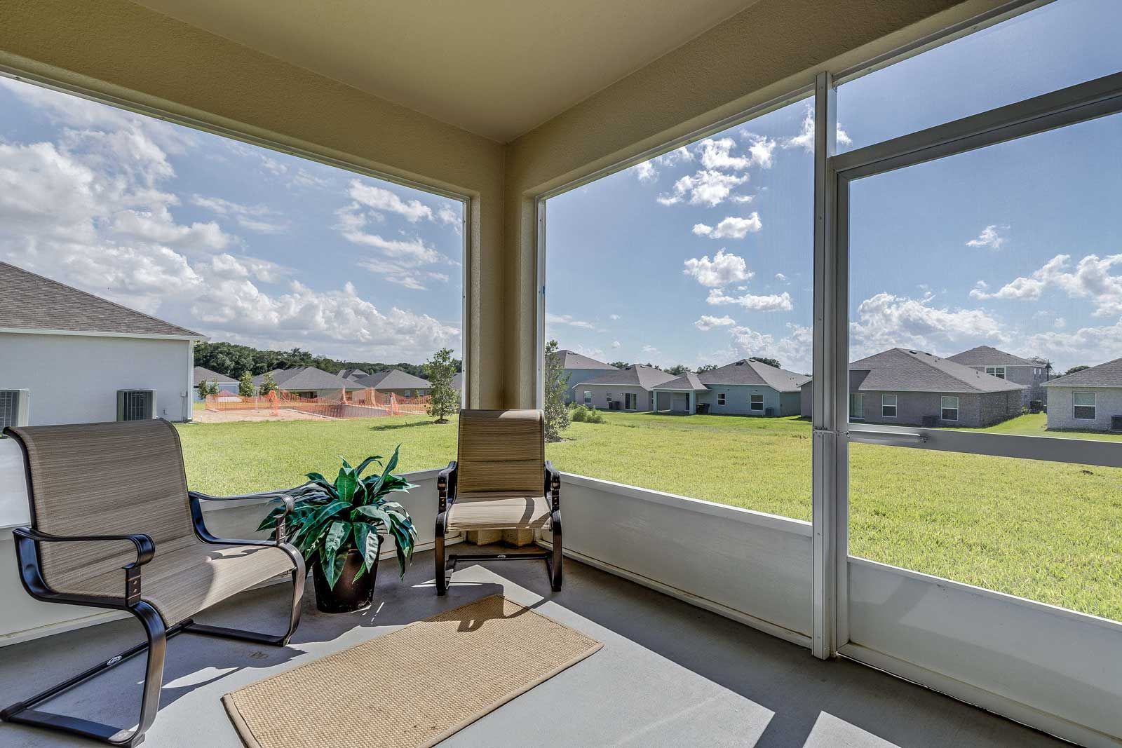 Screened porch with two chairs, potted plant, and outdoor view of houses and sky.