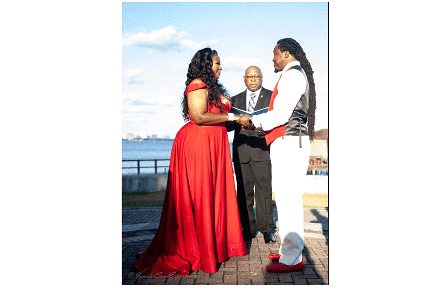 A man and a woman are holding hands during a wedding ceremony . the woman is wearing a red dress.
