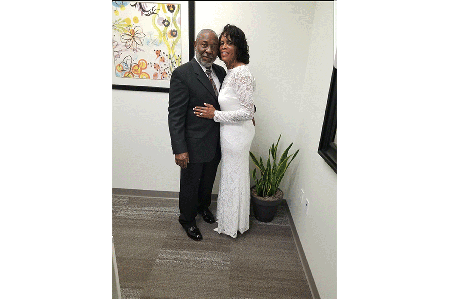 A man in a suit and a woman in a white dress are posing for a picture.