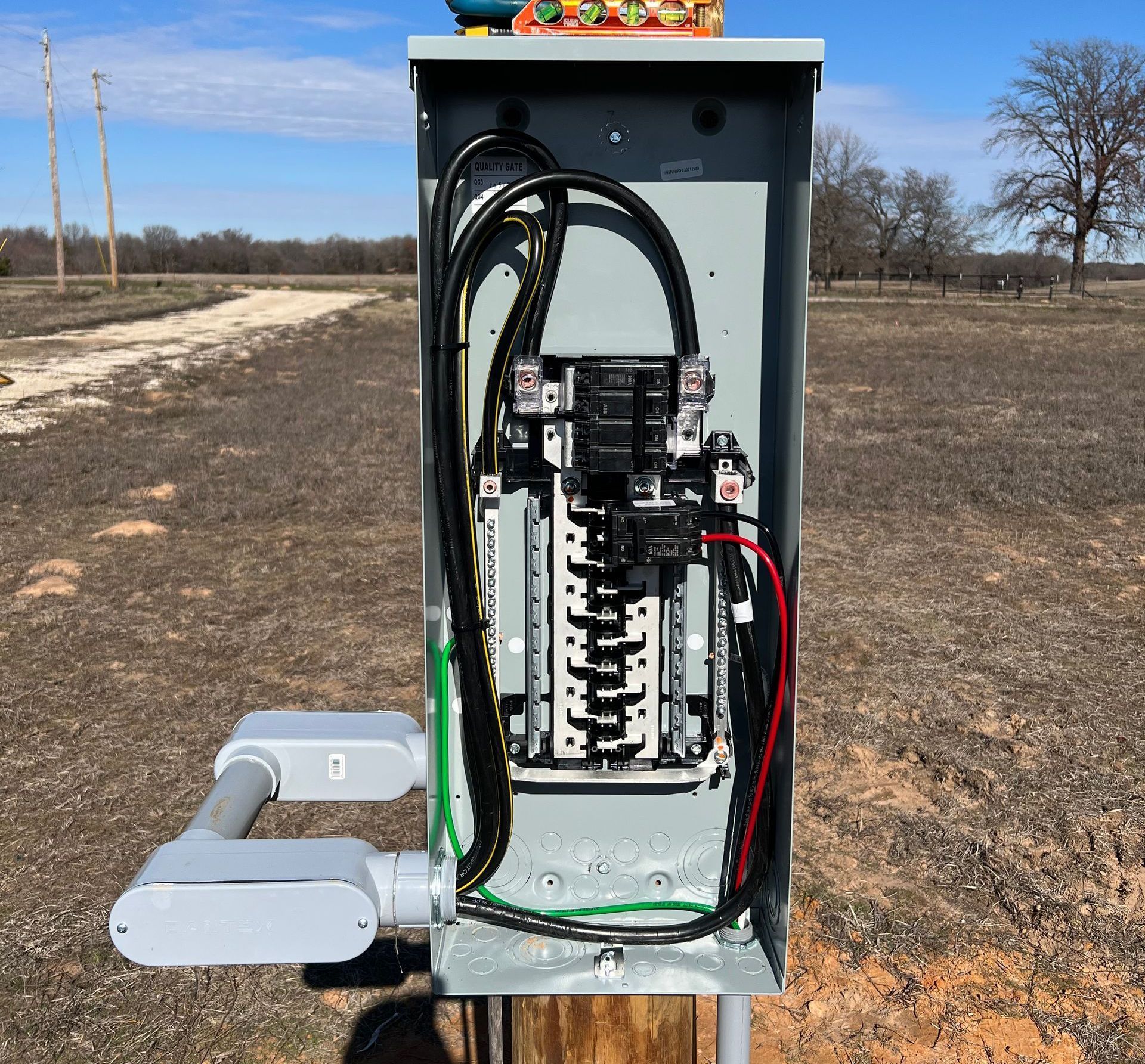 An electrical box is sitting on top of a wooden post in a field.