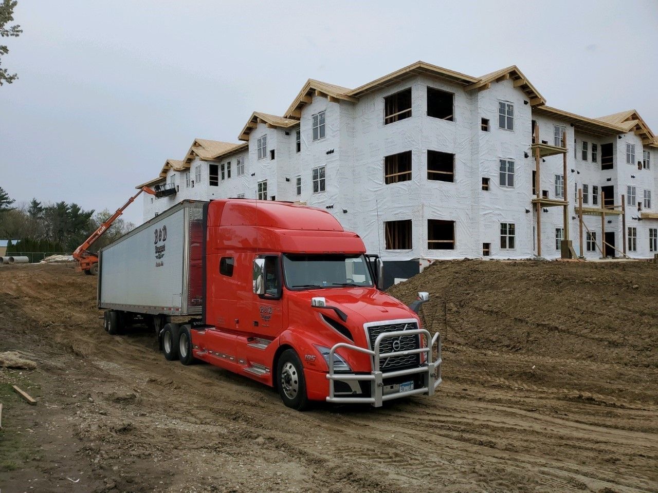 A red semi truck is parked in front of a building under construction.