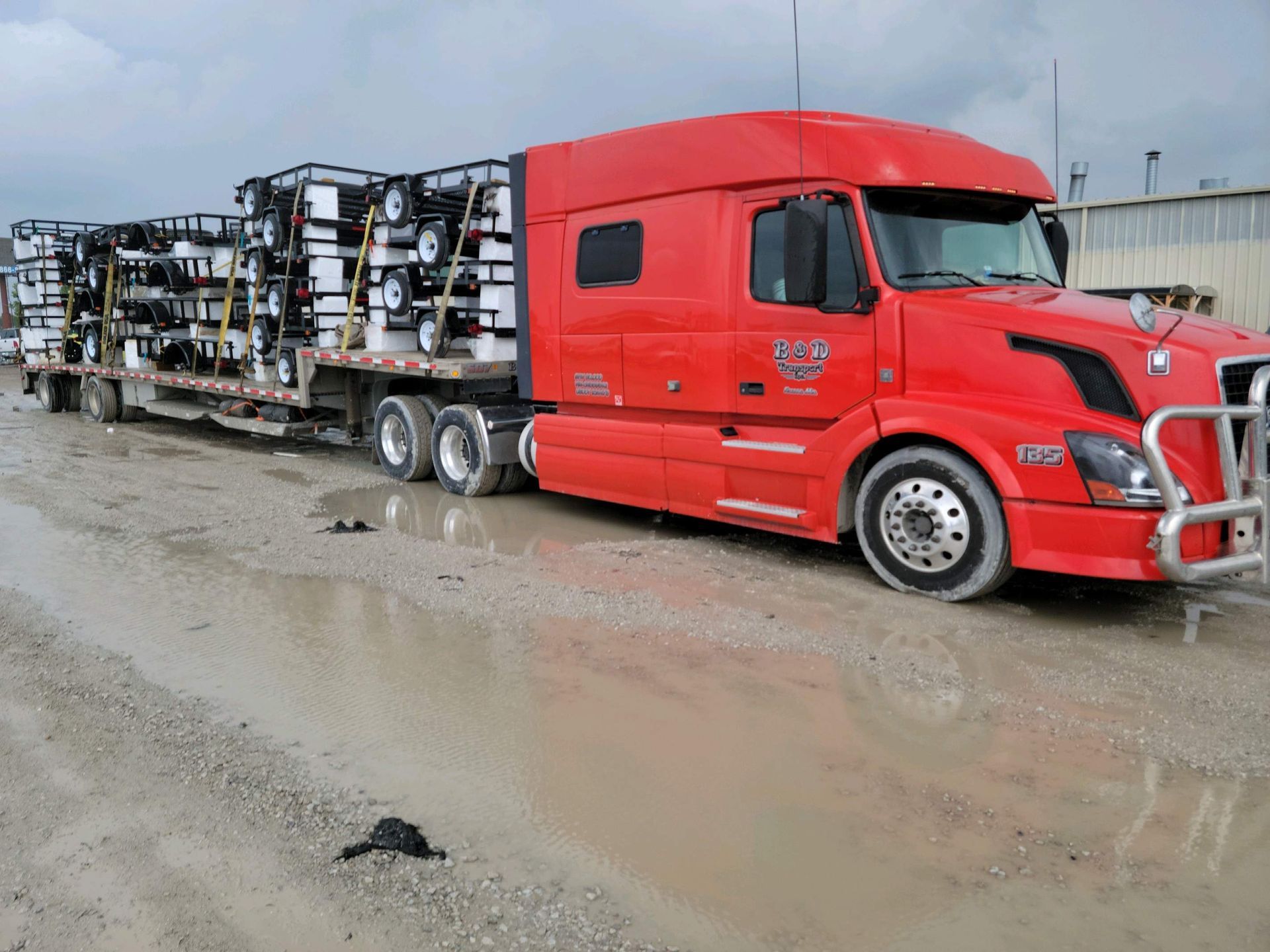 A red semi truck is parked on a muddy road.