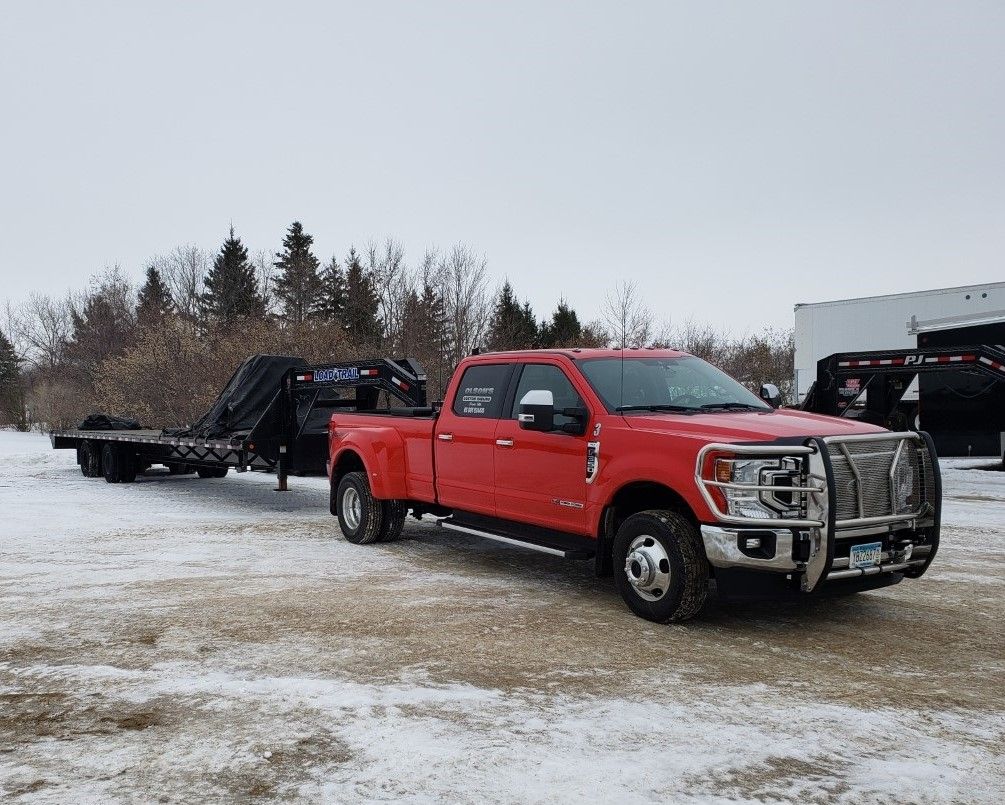 A red truck is towing a trailer in the snow.