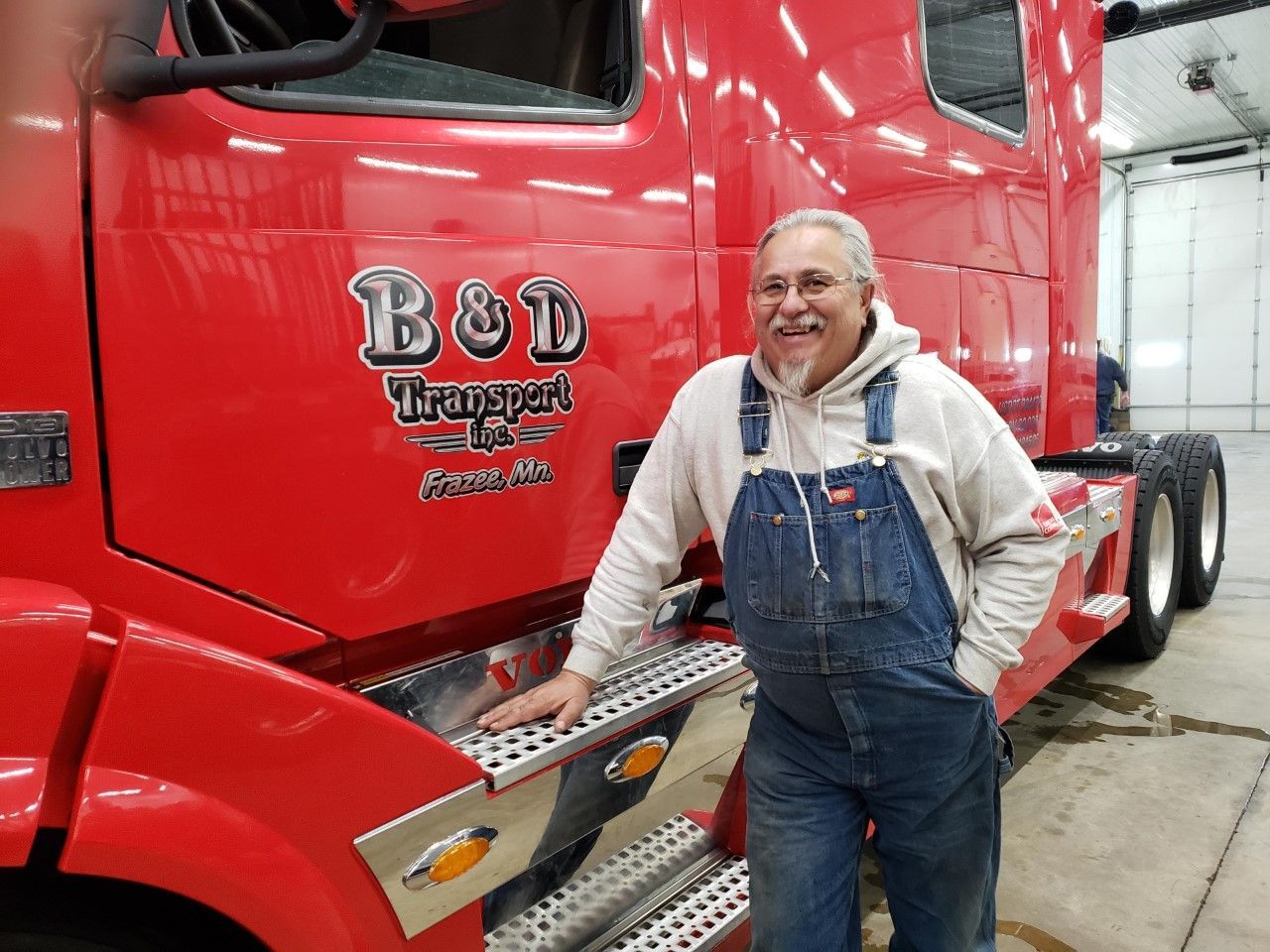 A man in overalls is standing in front of a red truck.