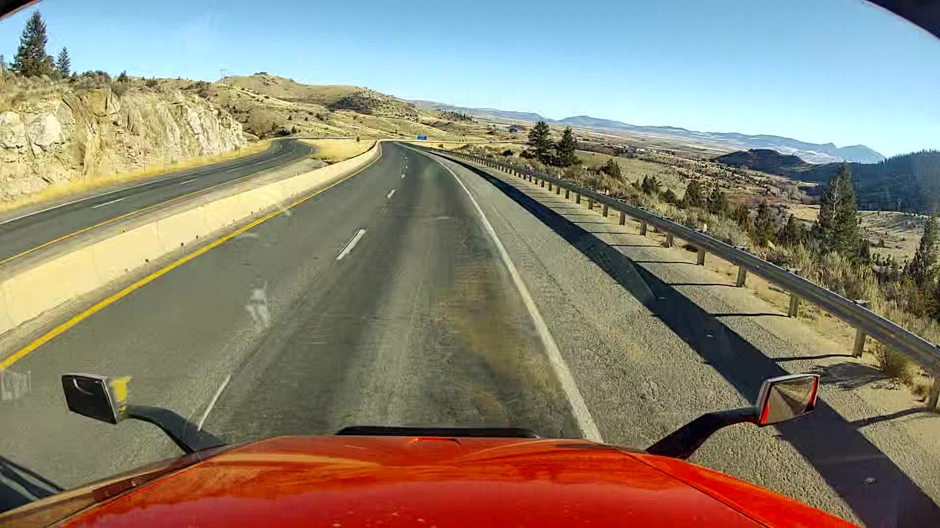 A red truck is driving down a highway with mountains in the background.