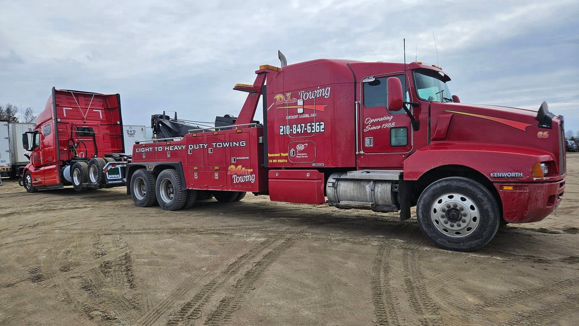 A red tow truck with a trailer attached to it is parked in a dirt field.