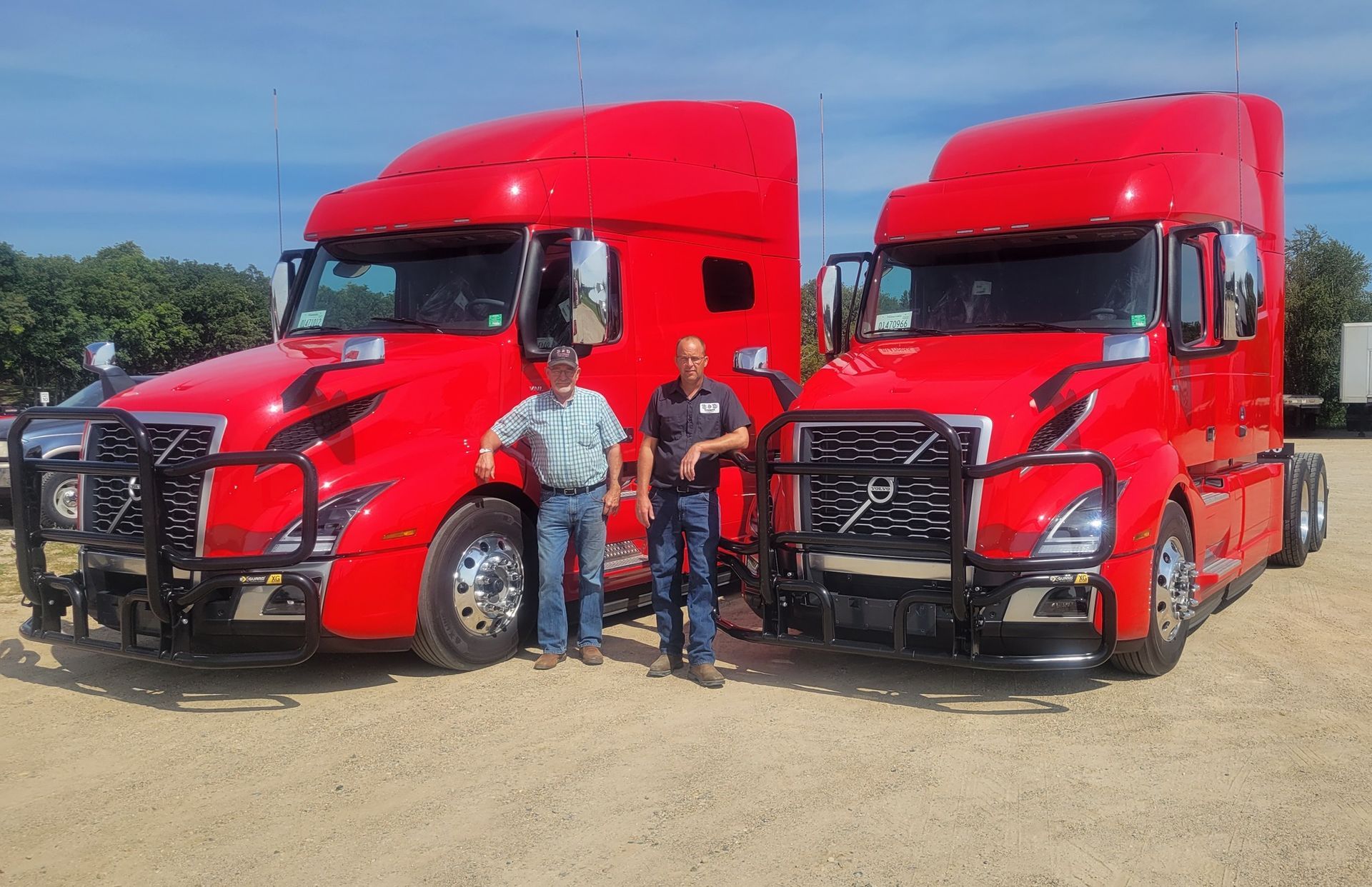 Two men are standing in front of two red semi trucks.