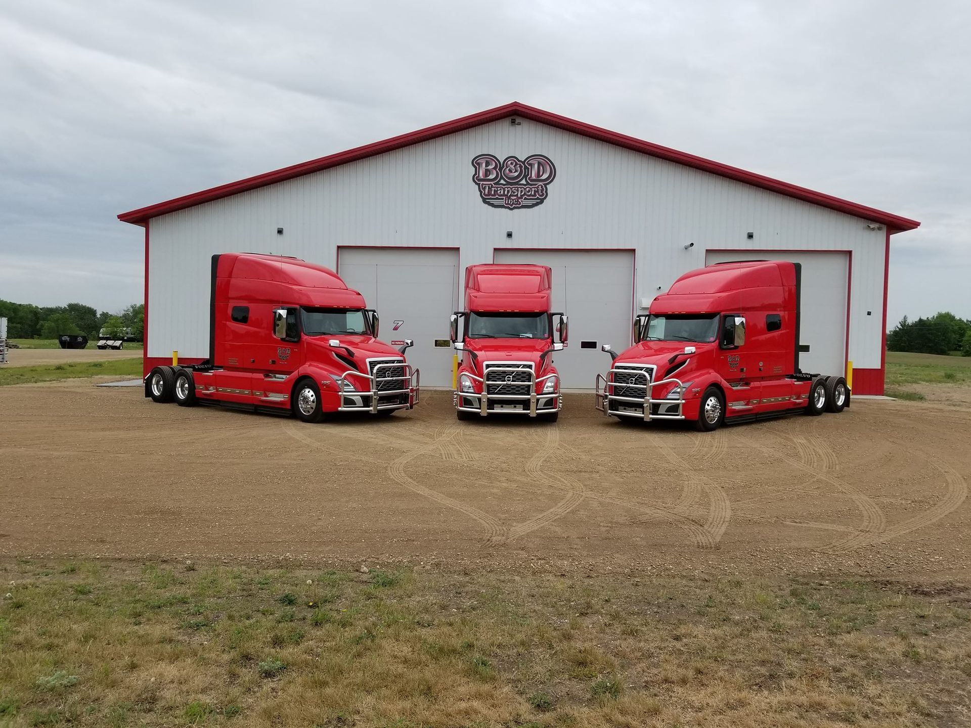 Three red semi trucks are parked in front of a white building.