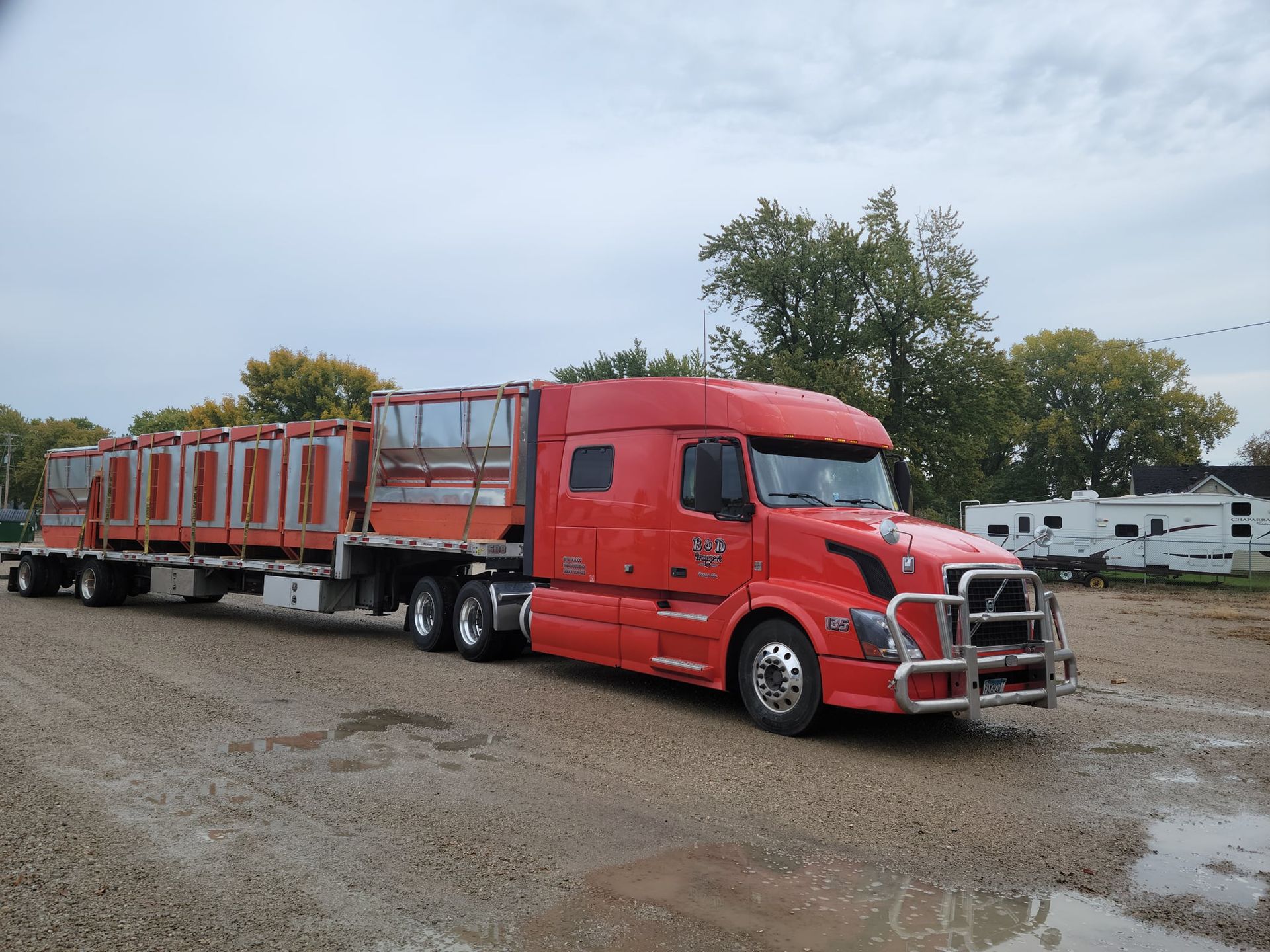 A red semi truck is parked in a gravel lot.