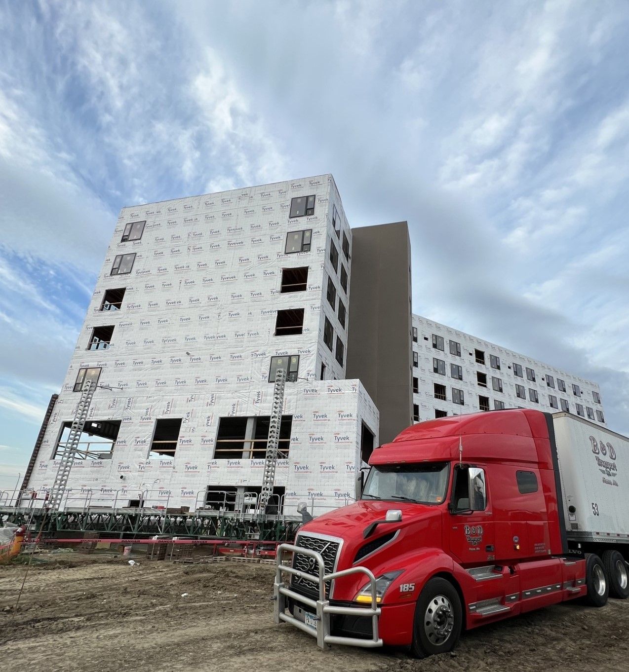 A red semi truck is parked in front of a building under construction.