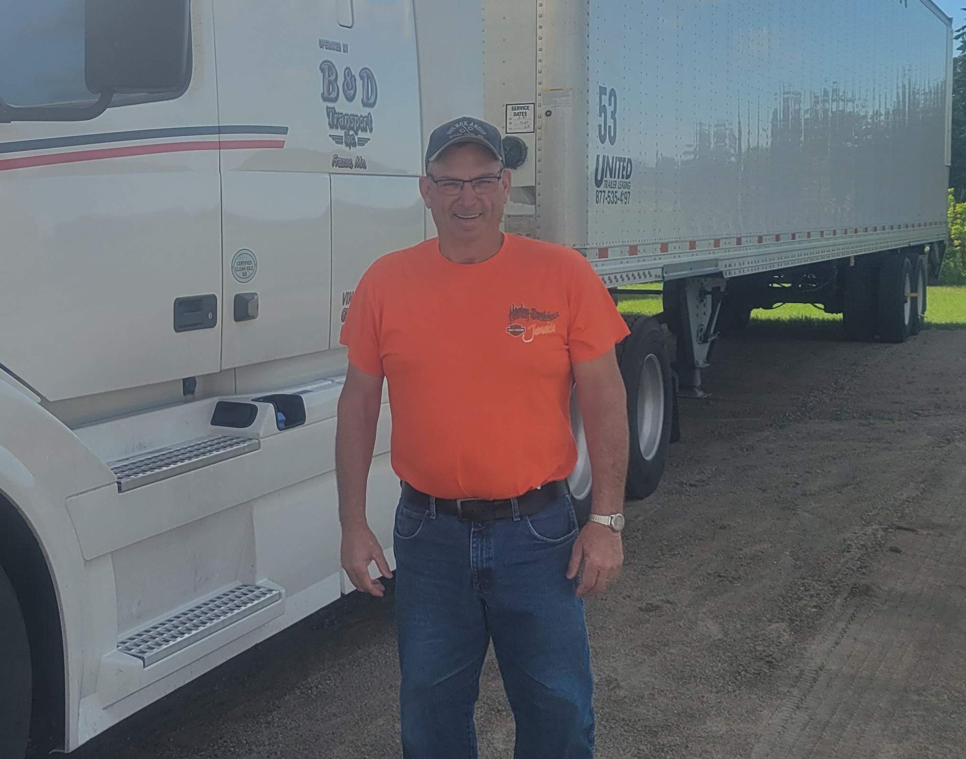 A man in an orange shirt is standing in front of a white semi truck.